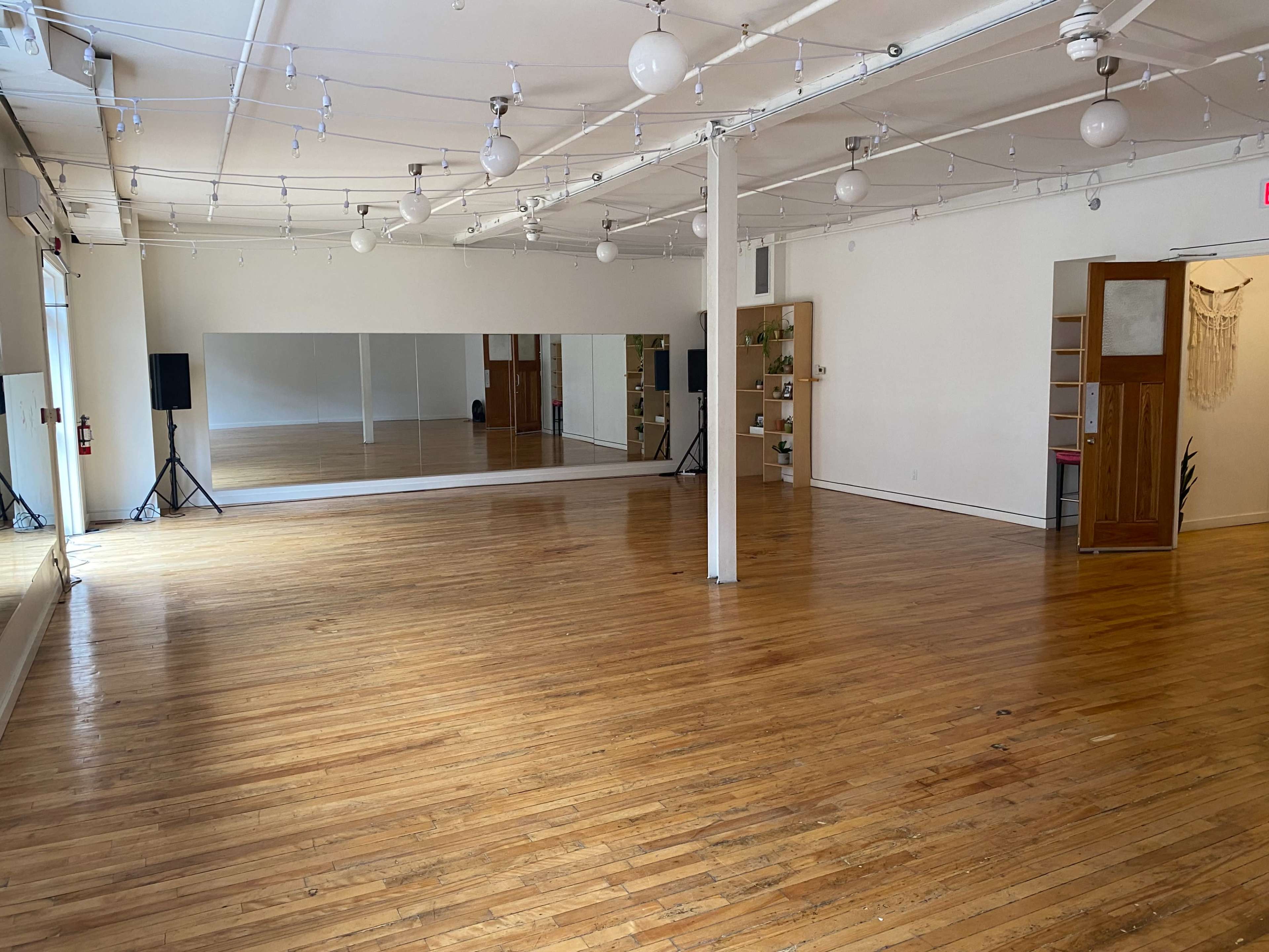 A spacious dance studio with polished wooden floors, large mirrors, and bright overhead lighting.