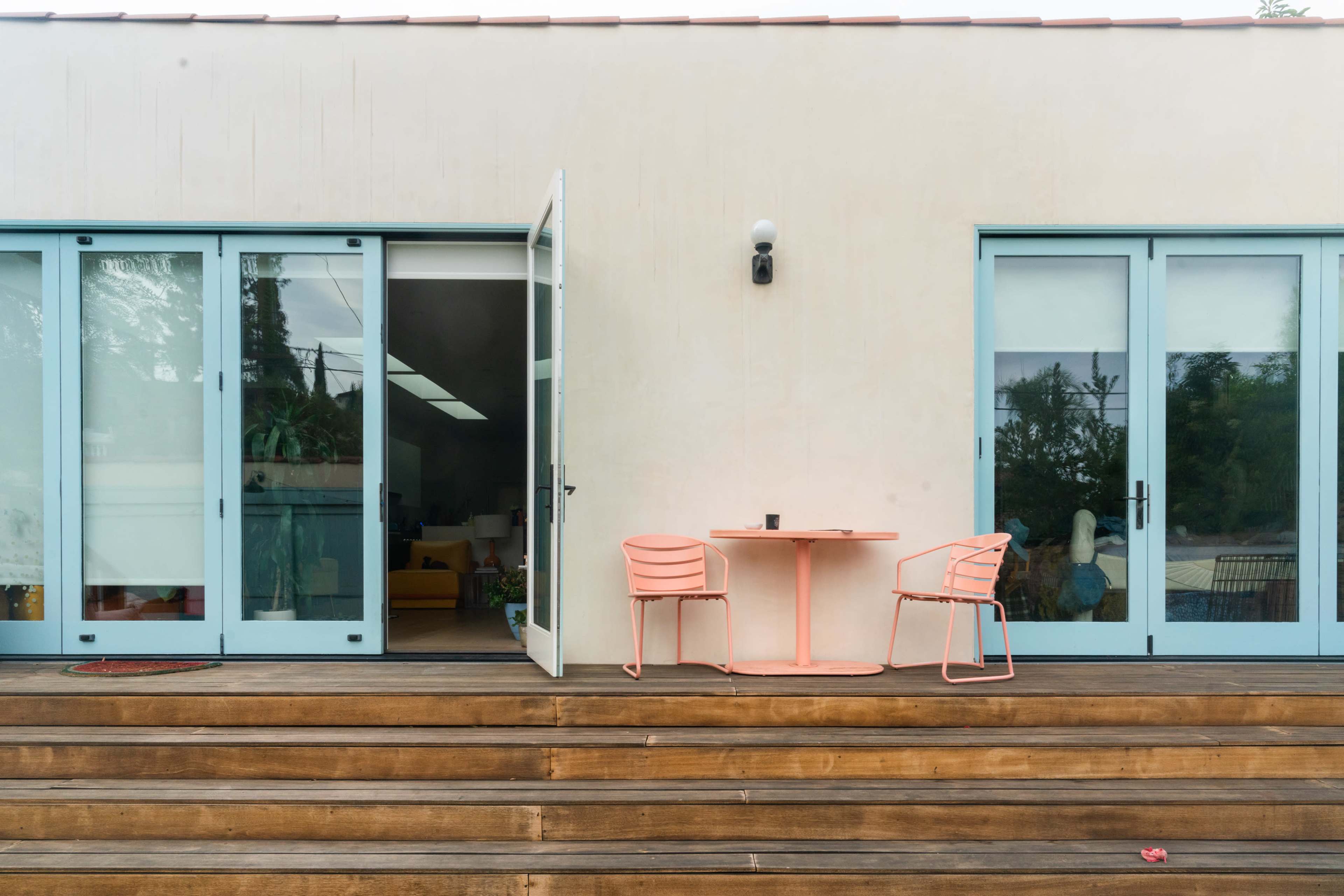 A modern patio with a light-colored building, a small round table, and two pink chairs, all situated on wooden steps.