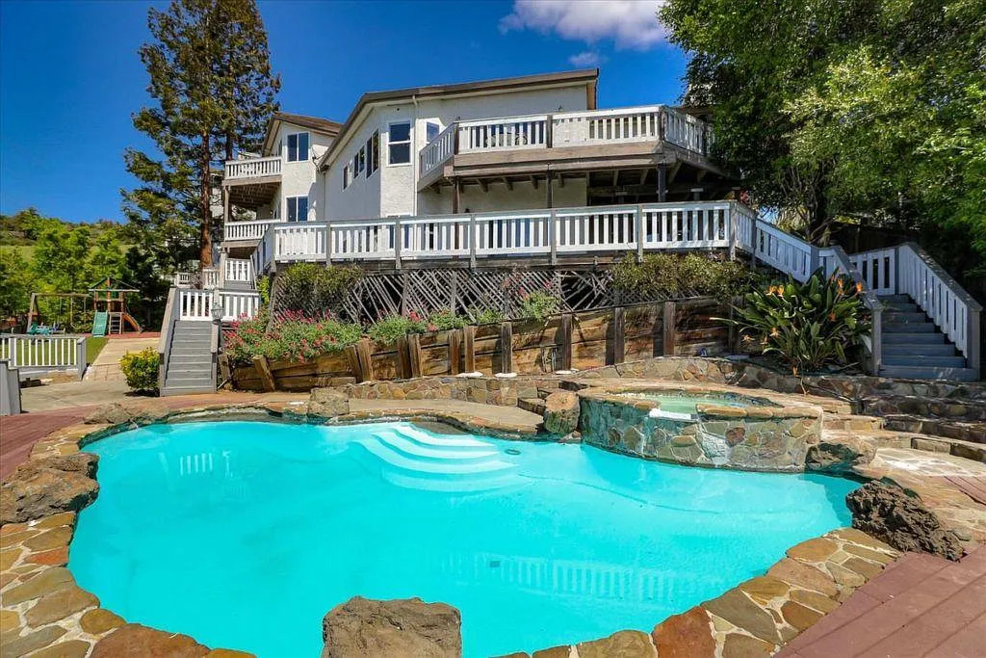 The image shows a house with multiple stories, a landscaped yard, and a swimming pool shaped like a heart, surrounded by stone borders.