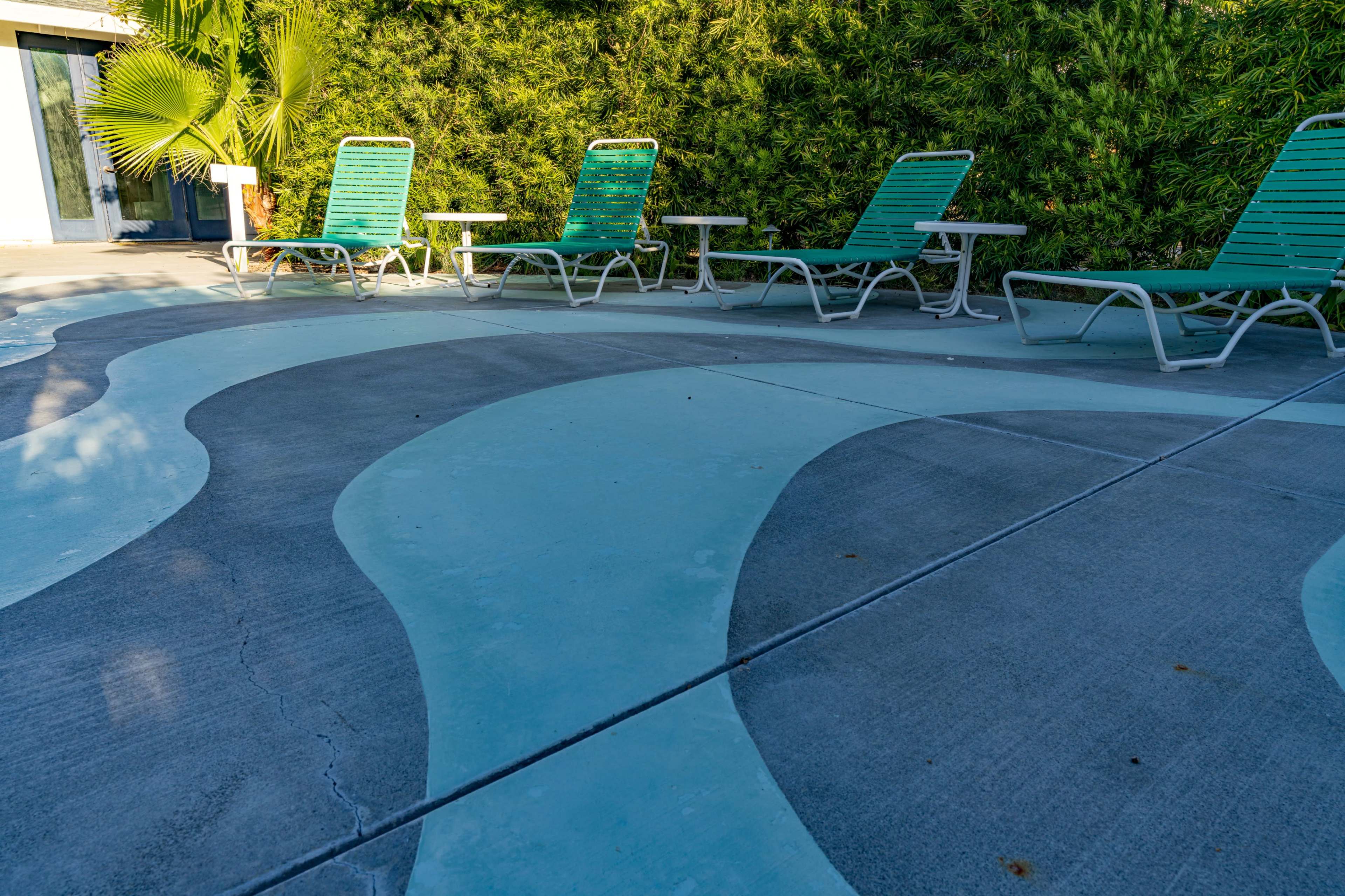 The image shows a poolside area with five green lounge chairs arranged around a patterned blue and gray concrete surface.