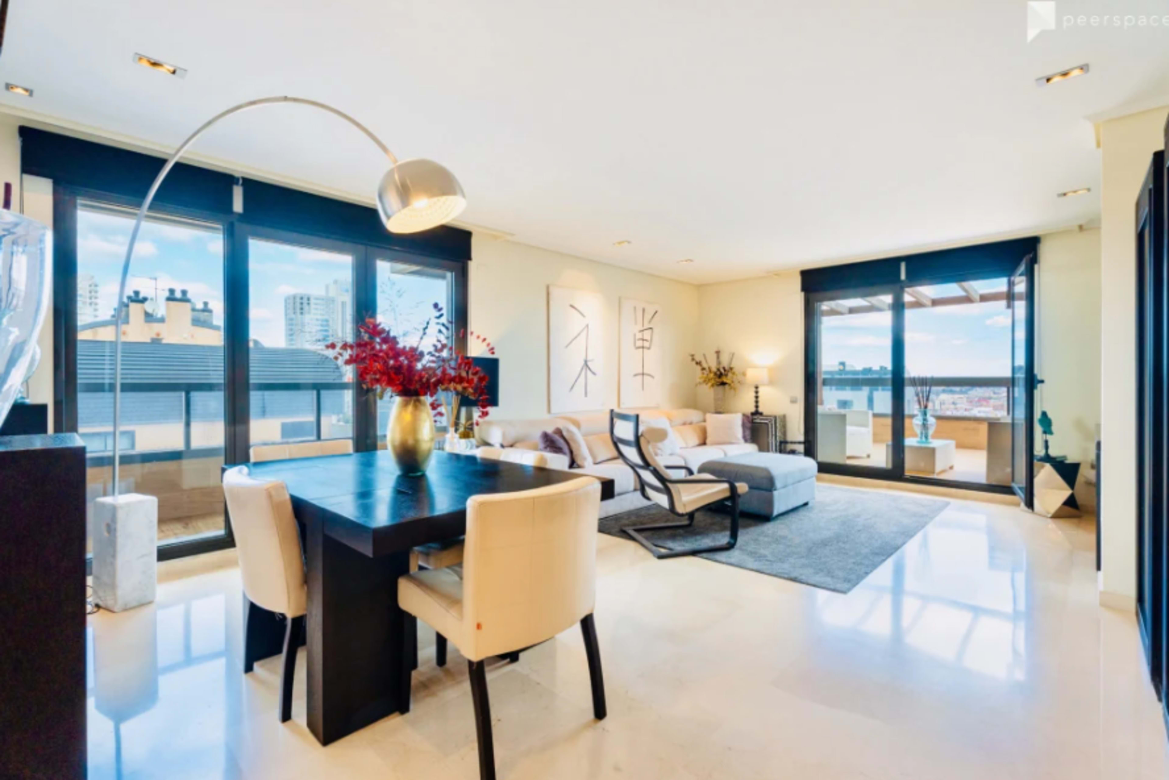 The image showcases a modern, spacious living area with large windows, a comfortable sofa, and a dining table set for four.