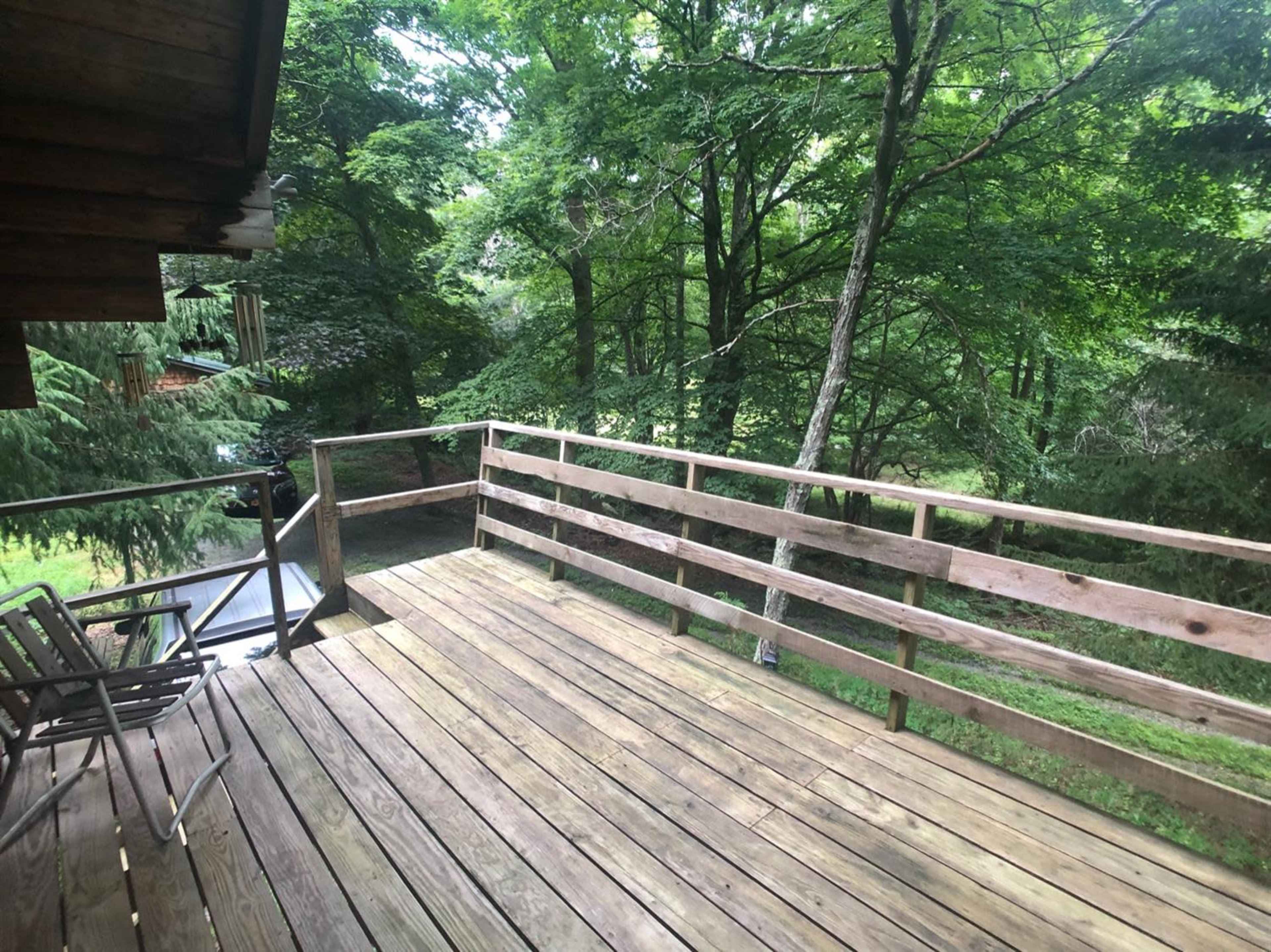 A wooden deck with chairs overlooks a densely wooded area.