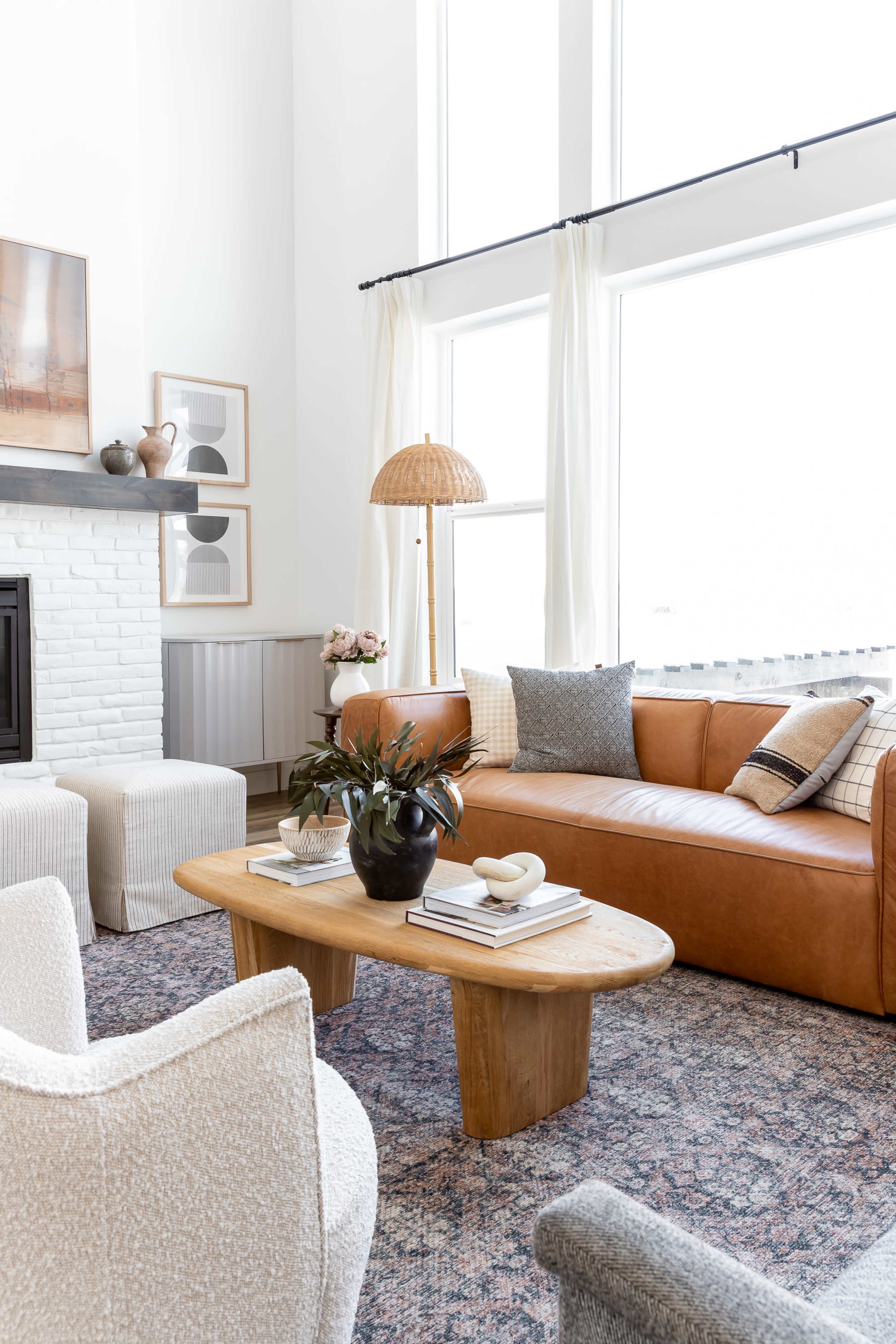 The living room features a combination of a leather sofa, modern chairs, a wooden coffee table, and large windows allowing natural light.