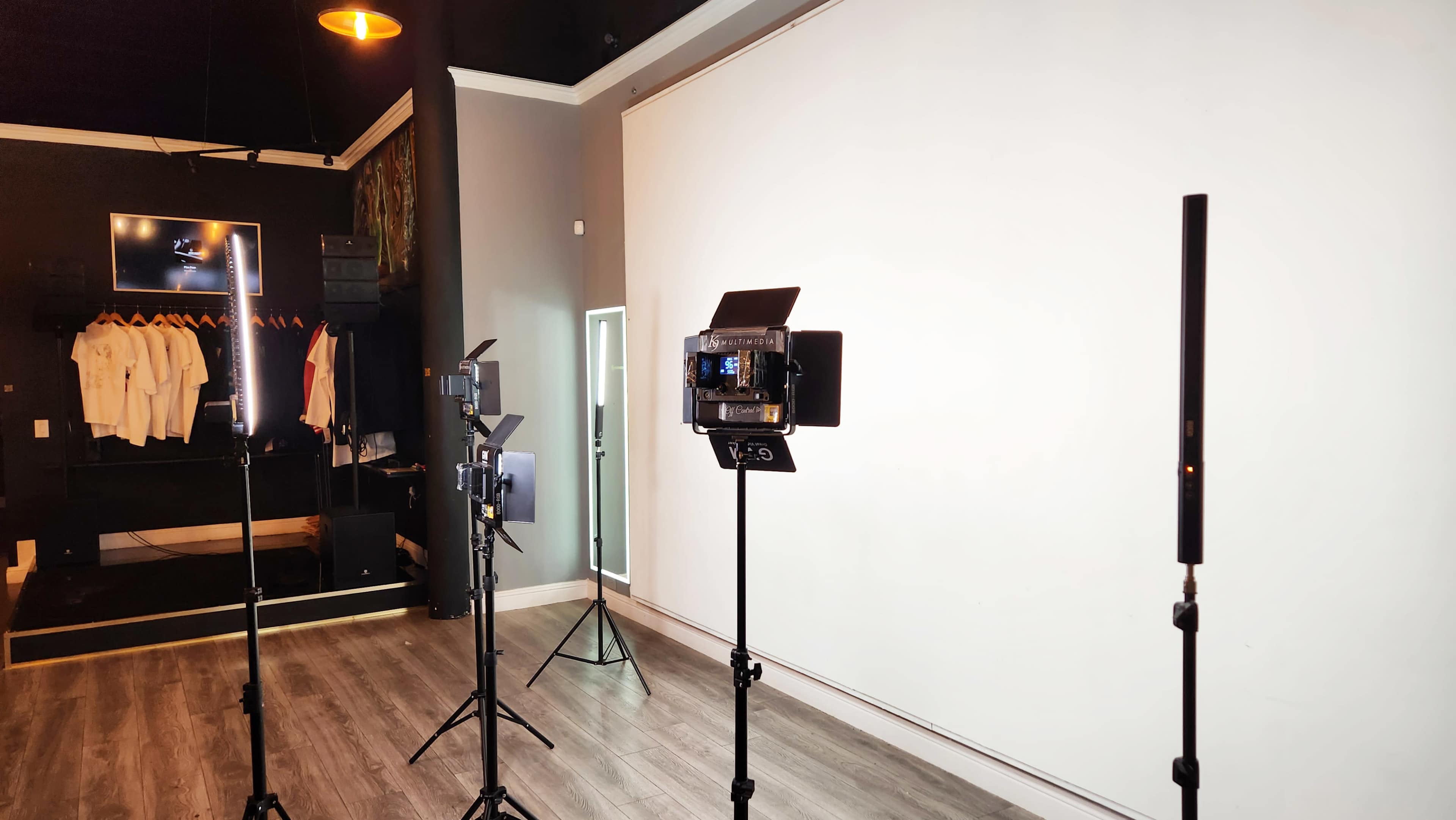 A photography studio with lighting equipment on tripods arranged in front of a large white backdrop and a black wall.