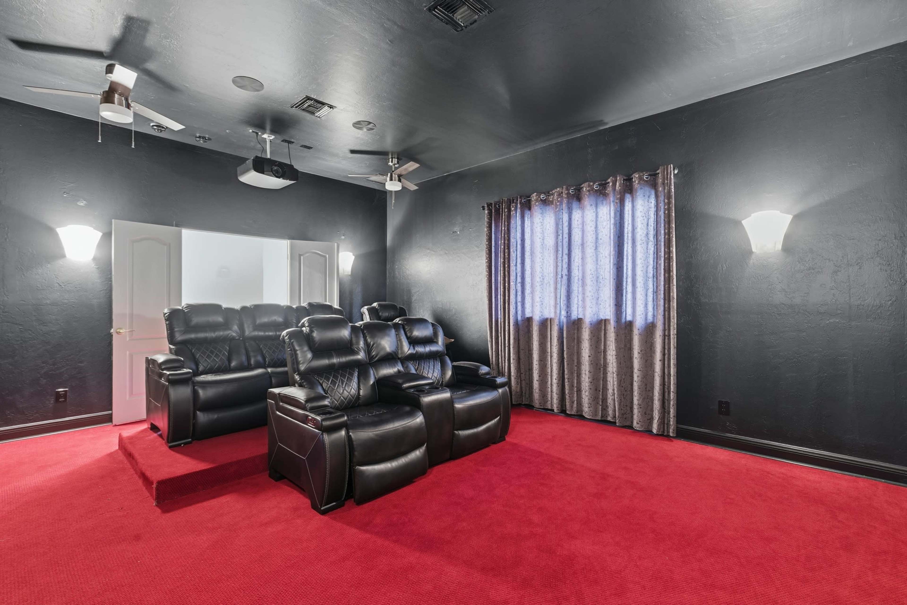 The image shows a home theater room with black walls, red carpeting, leather seating, and a window covered by sheer curtains.