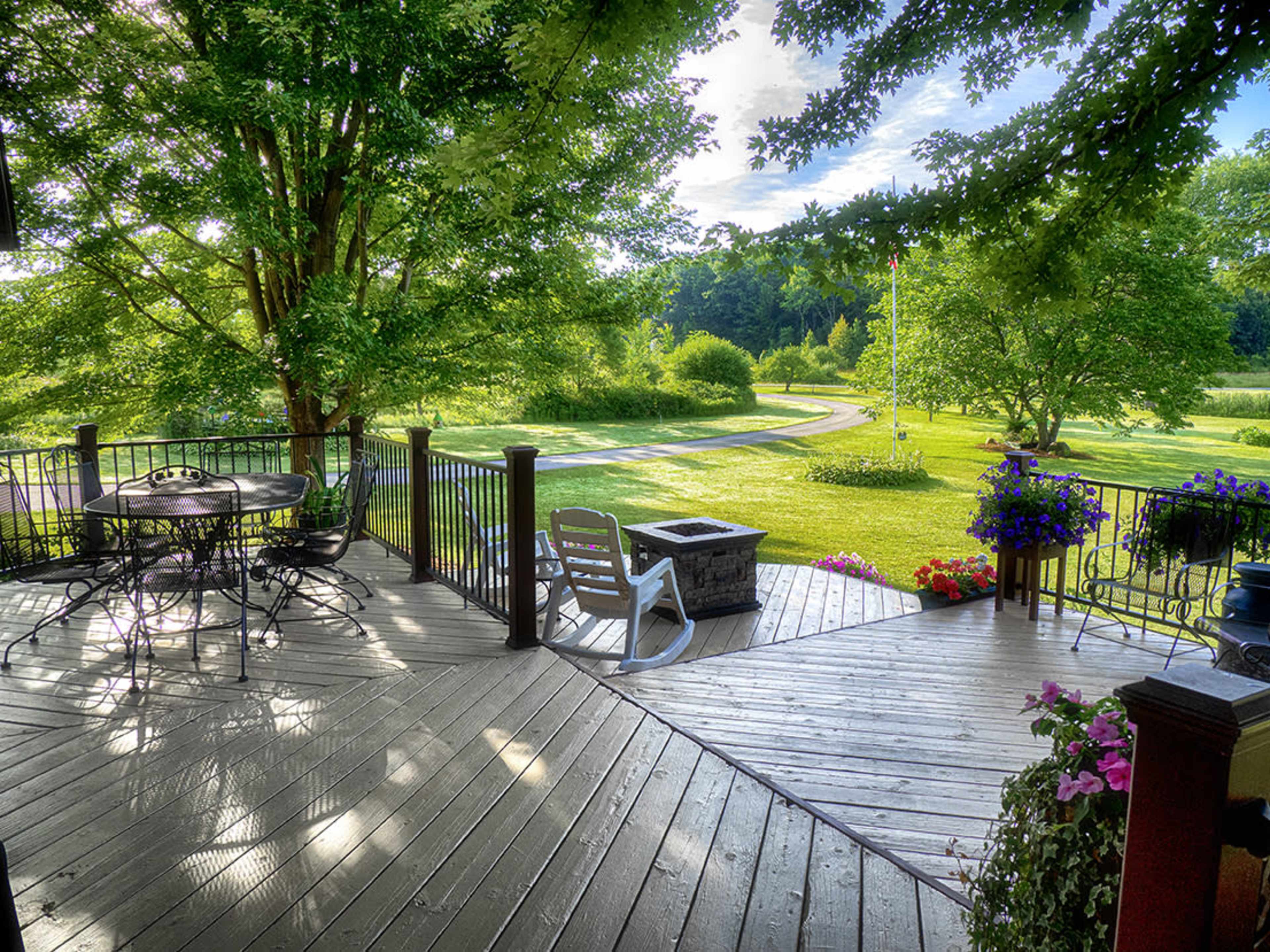 A wooden deck overlooks a lush green landscape with trees and a winding path.