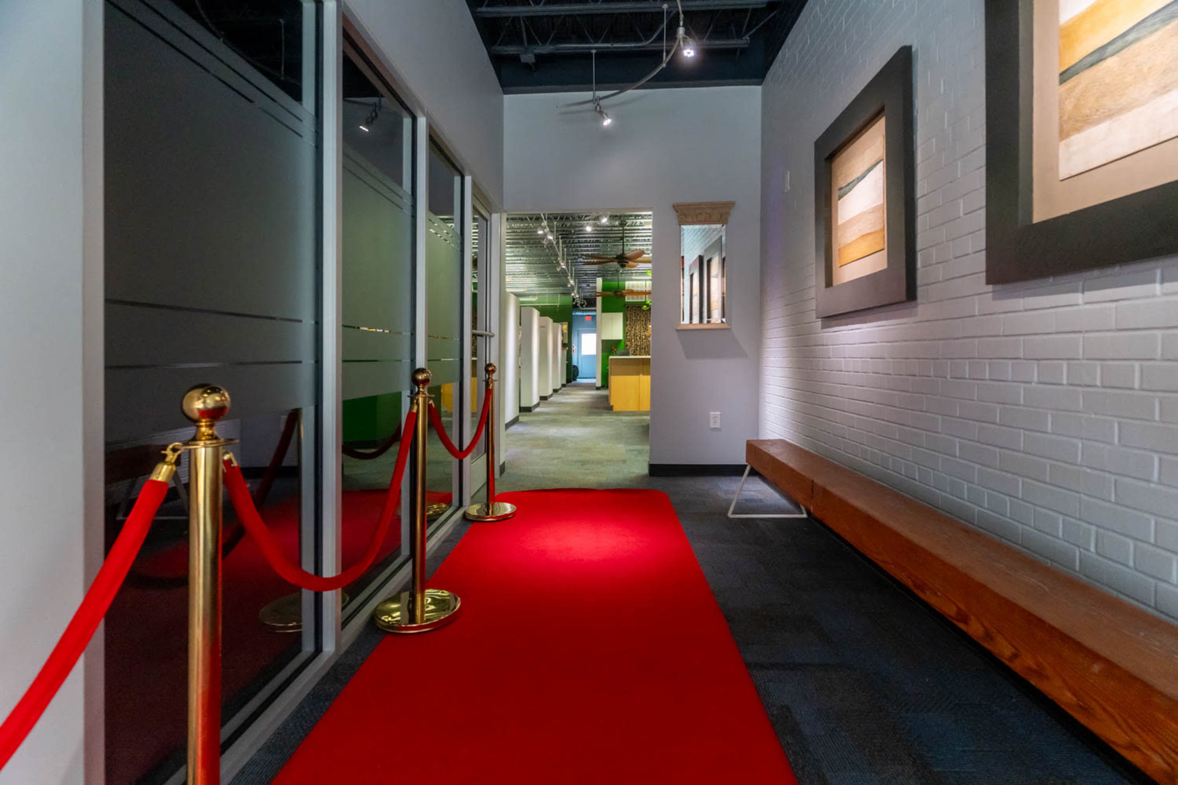 A hallway with a red carpet, lined by stanchions, leading to several offices and illuminated by overhead lights.