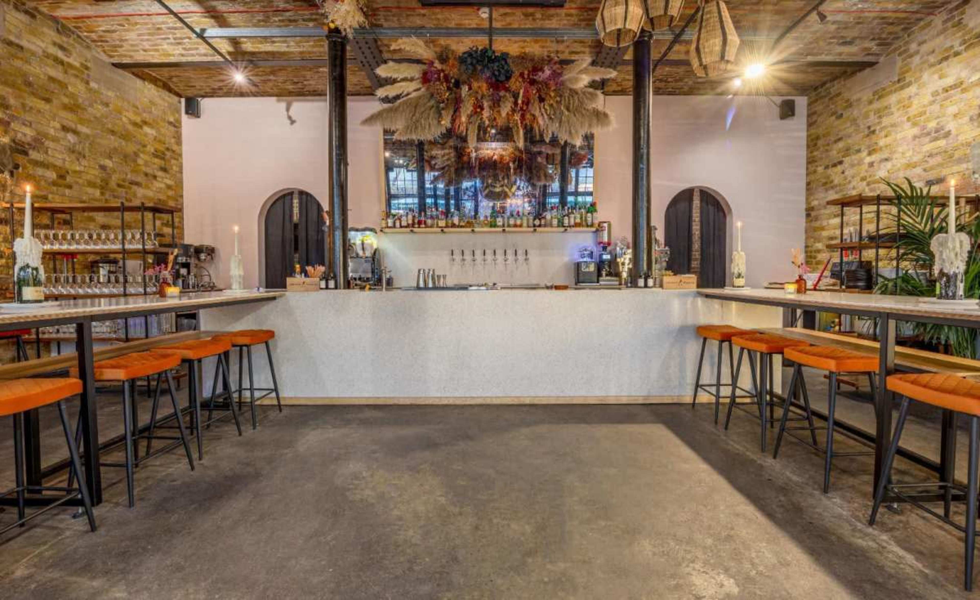 A modern bar with a white countertop, orange barstools, and a decorative arrangement of dried foliage hanging from the ceiling.