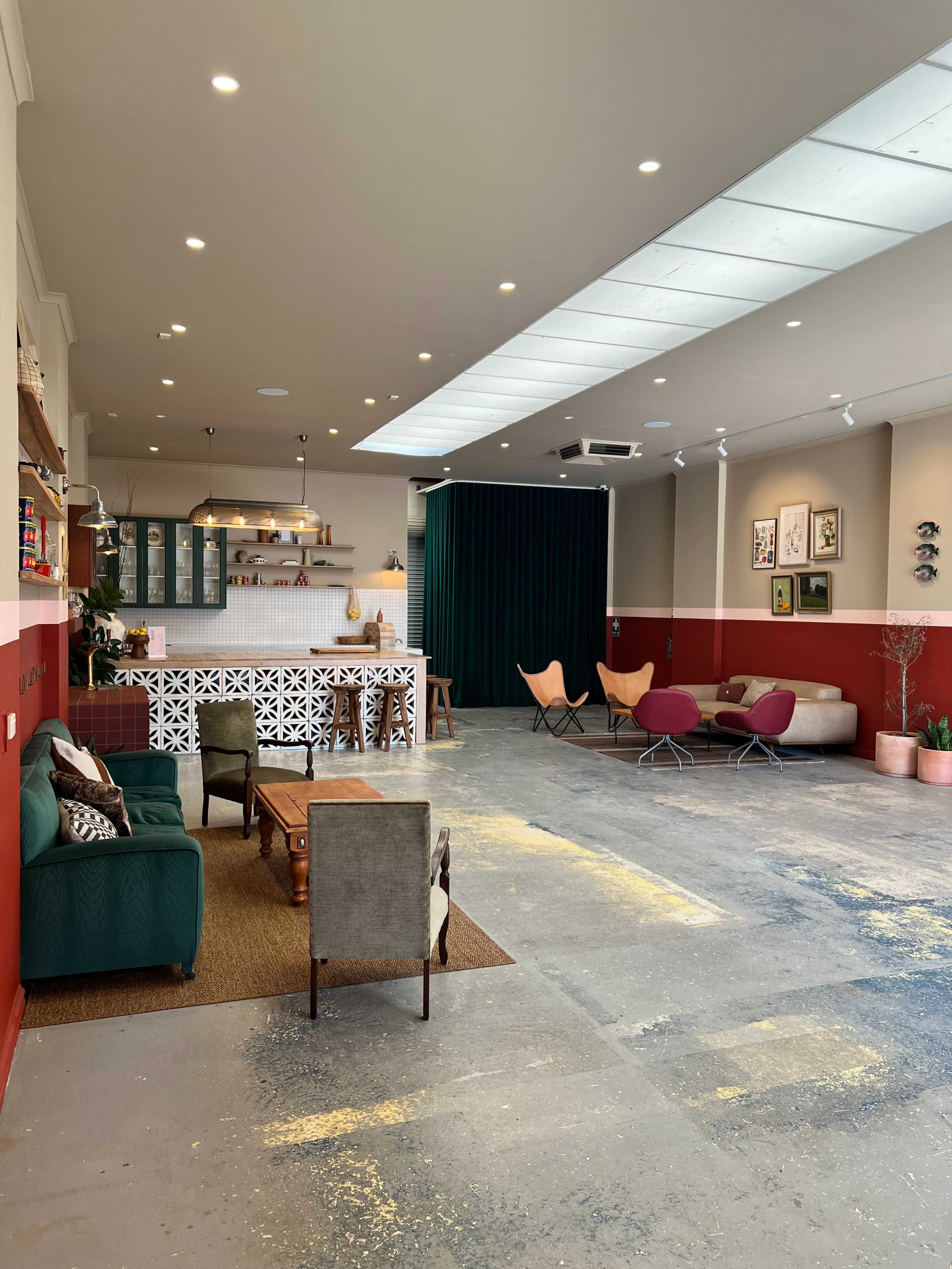 The image shows a stylish, modern interior with a mix of green and red walls, featuring a seating area with various furniture pieces and a spacious layout.