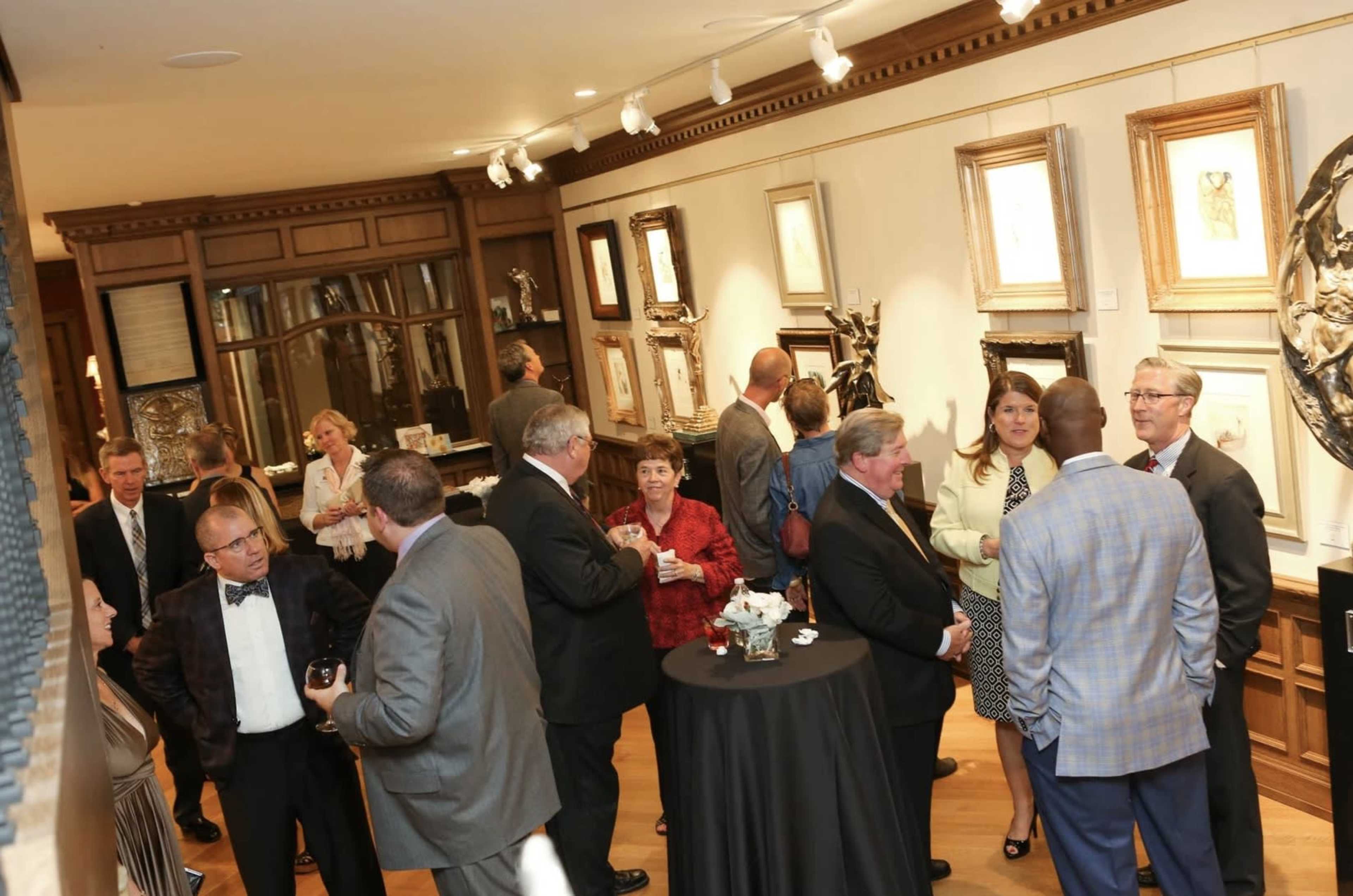 A group of people mingles at a gallery opening, surrounded by artwork and elegant decor.