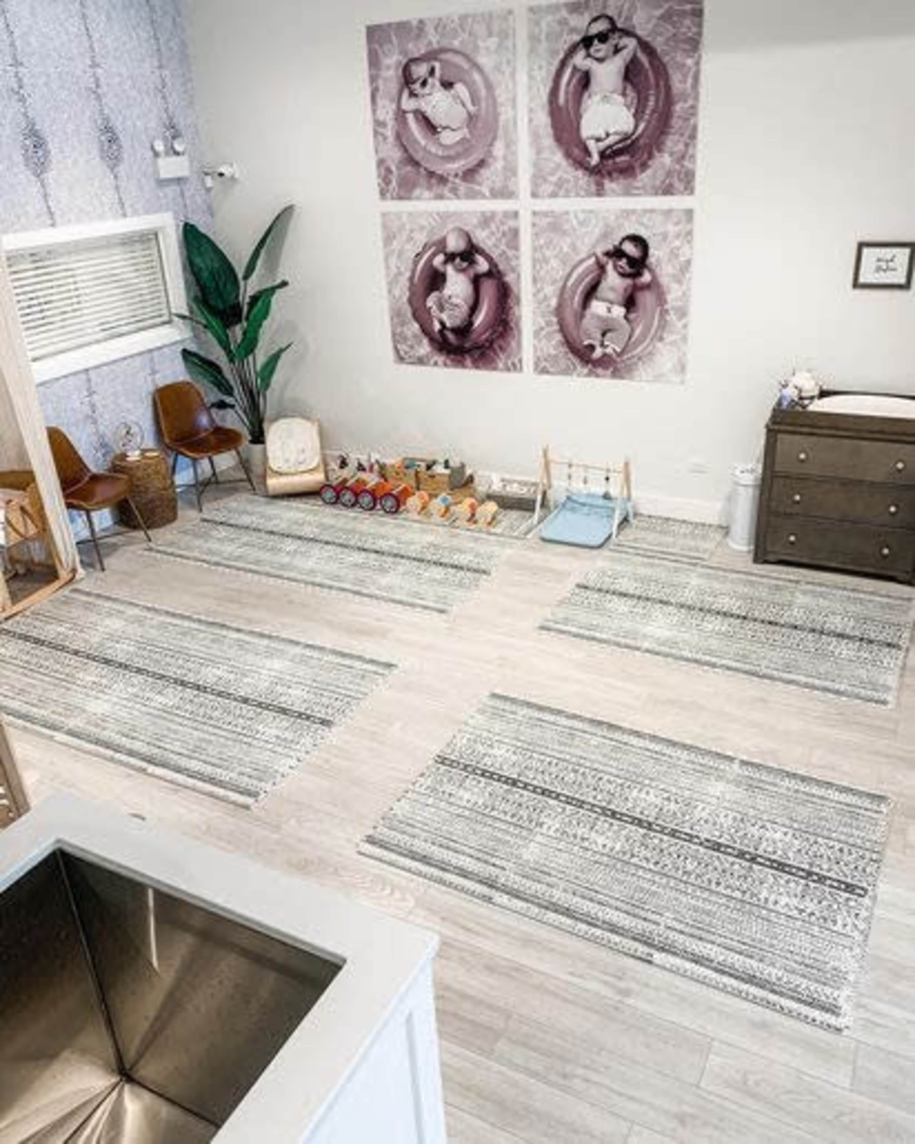 A light-filled room with patterned rugs, a dresser, plants, and framed photographs of children on the wall.
