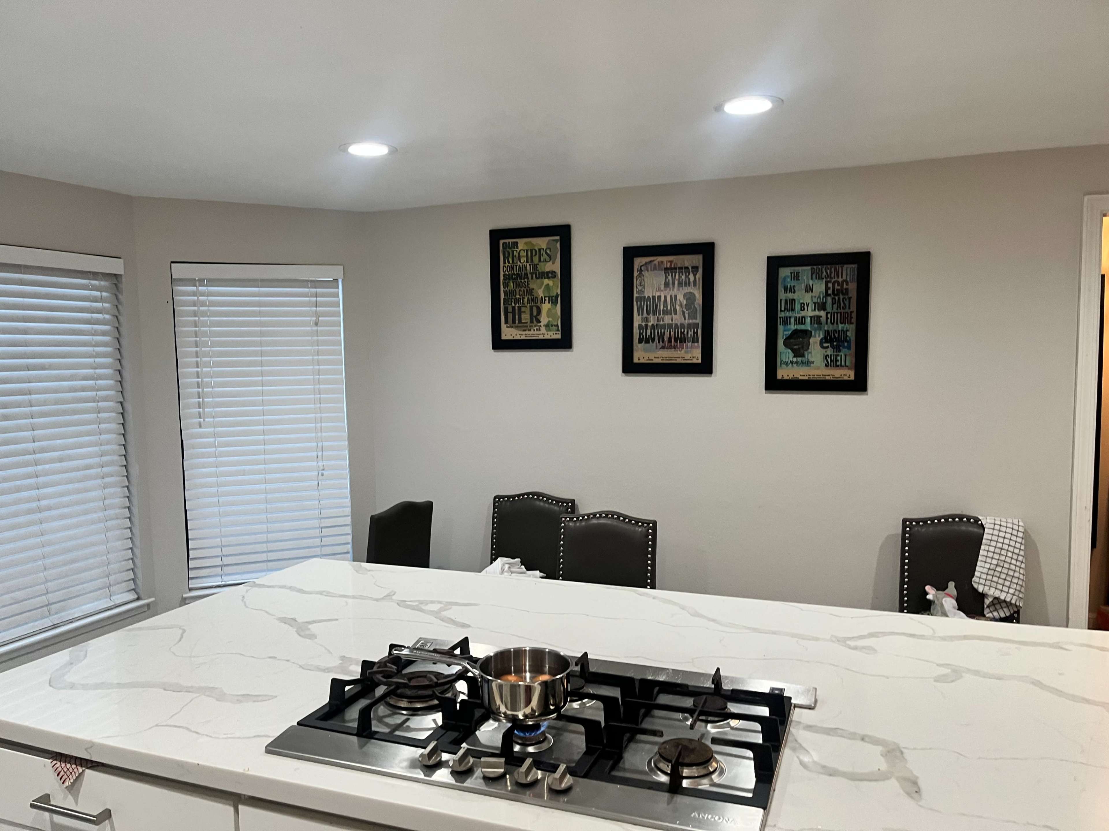 A modern kitchen with a marble countertop, a gas stove with a pot on it, and three framed artworks hanging on the wall.