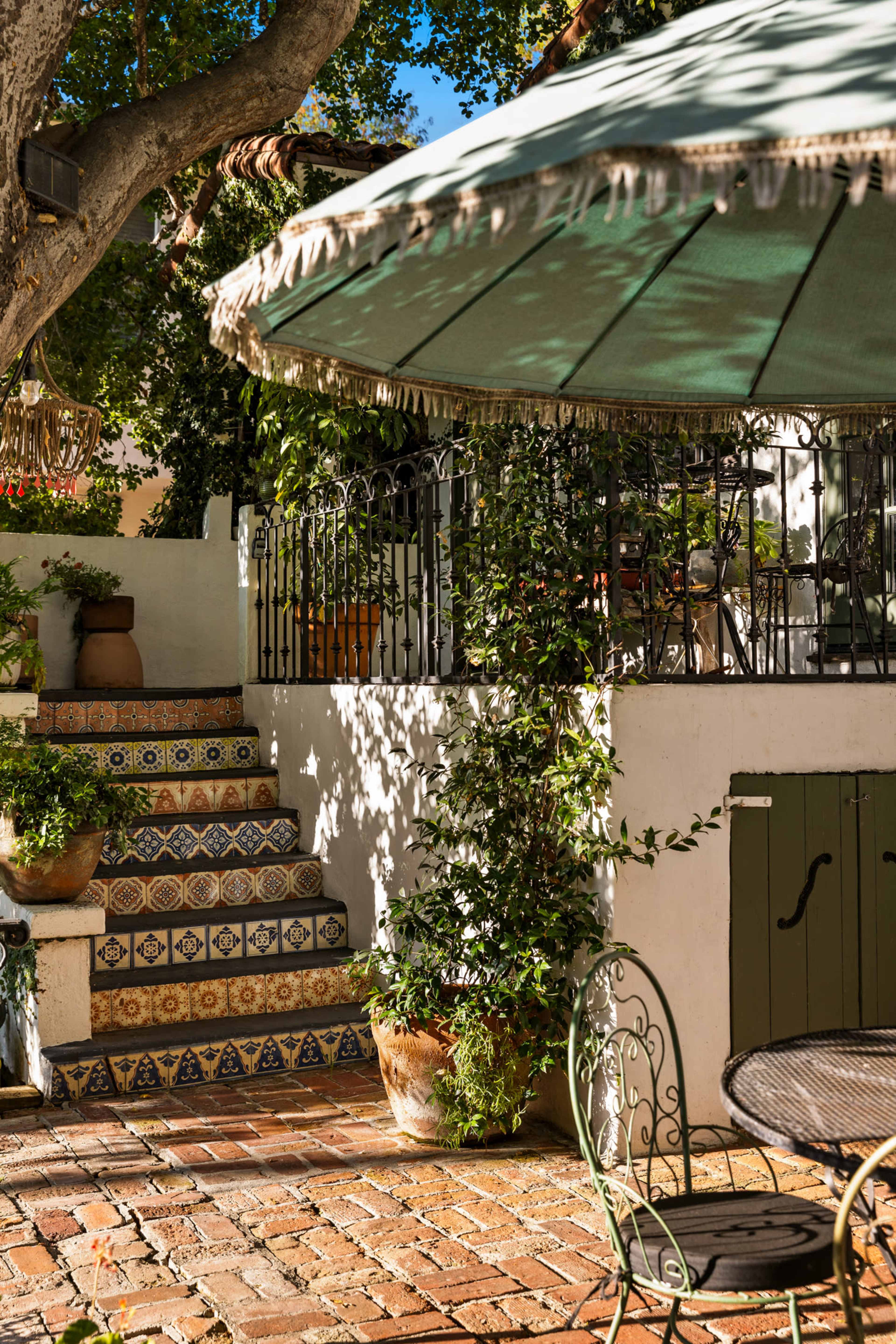 A shaded patio features a set of colorful tiled stairs bordered by greenery and various potted plants.