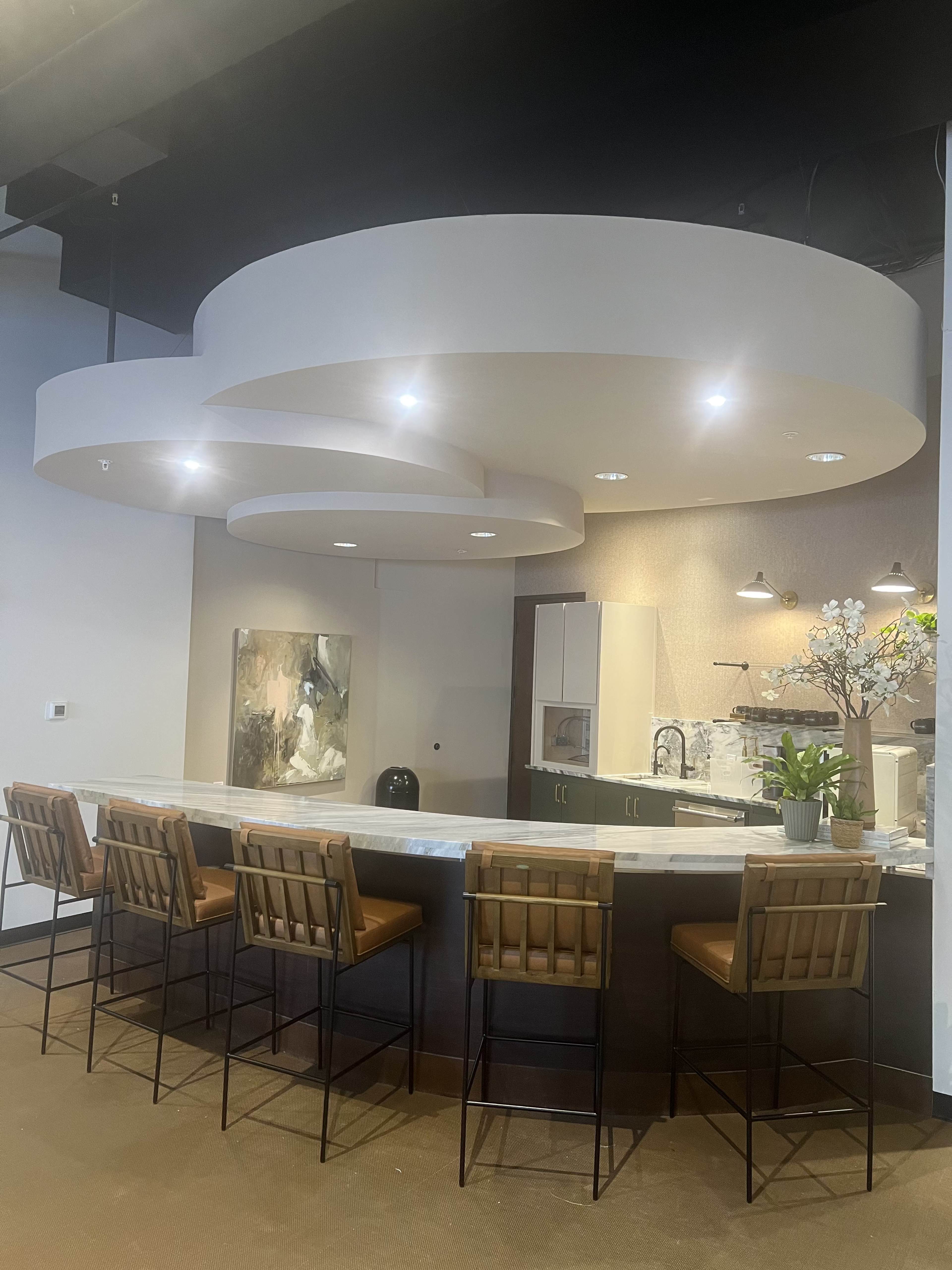 A modern kitchen bar area features a curved ceiling design, light fixtures, and seating with brown leather stools.