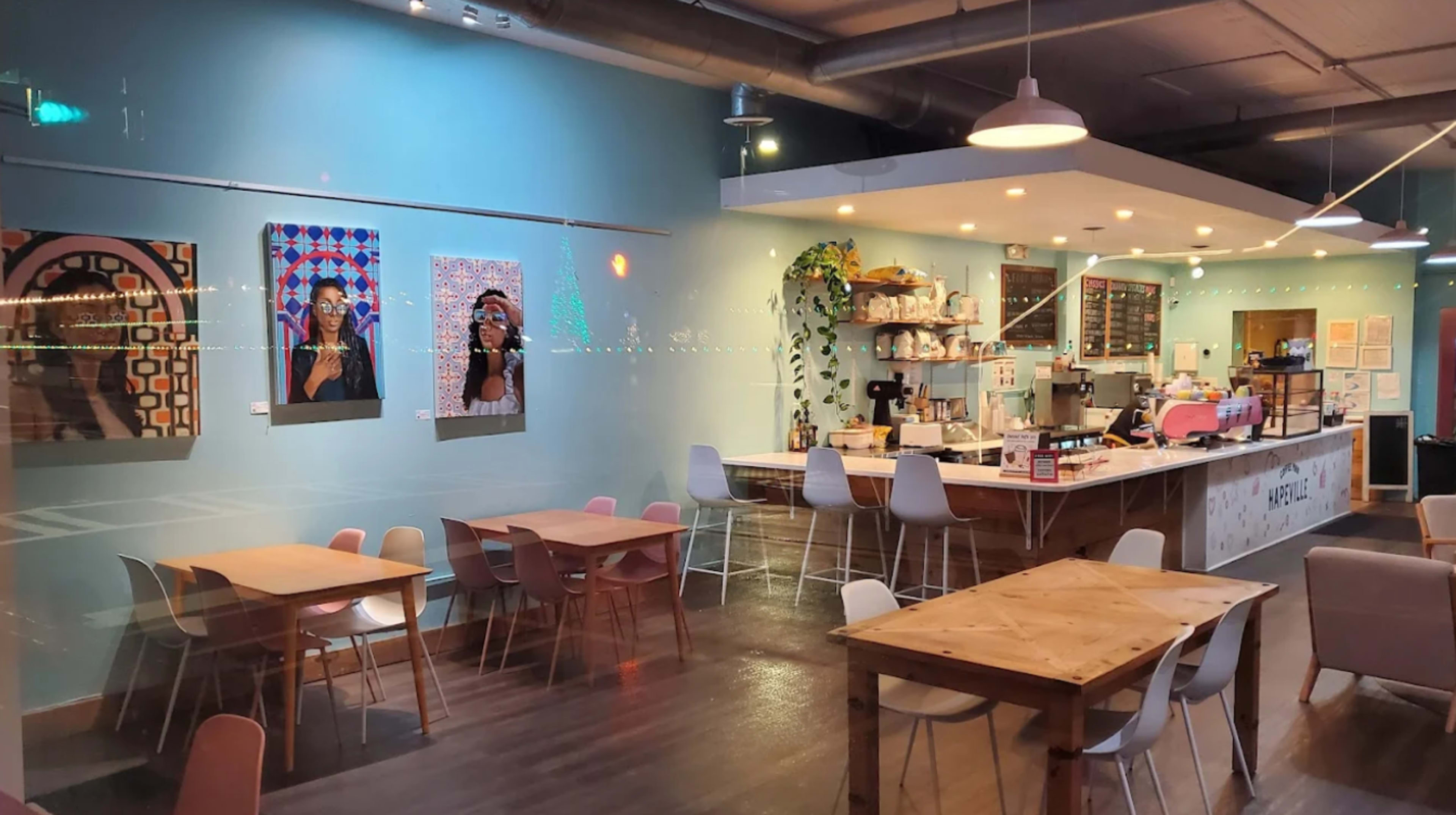 The image shows a café interior with colorful artwork on the walls, wooden tables, and a counter displaying various food and drink items.