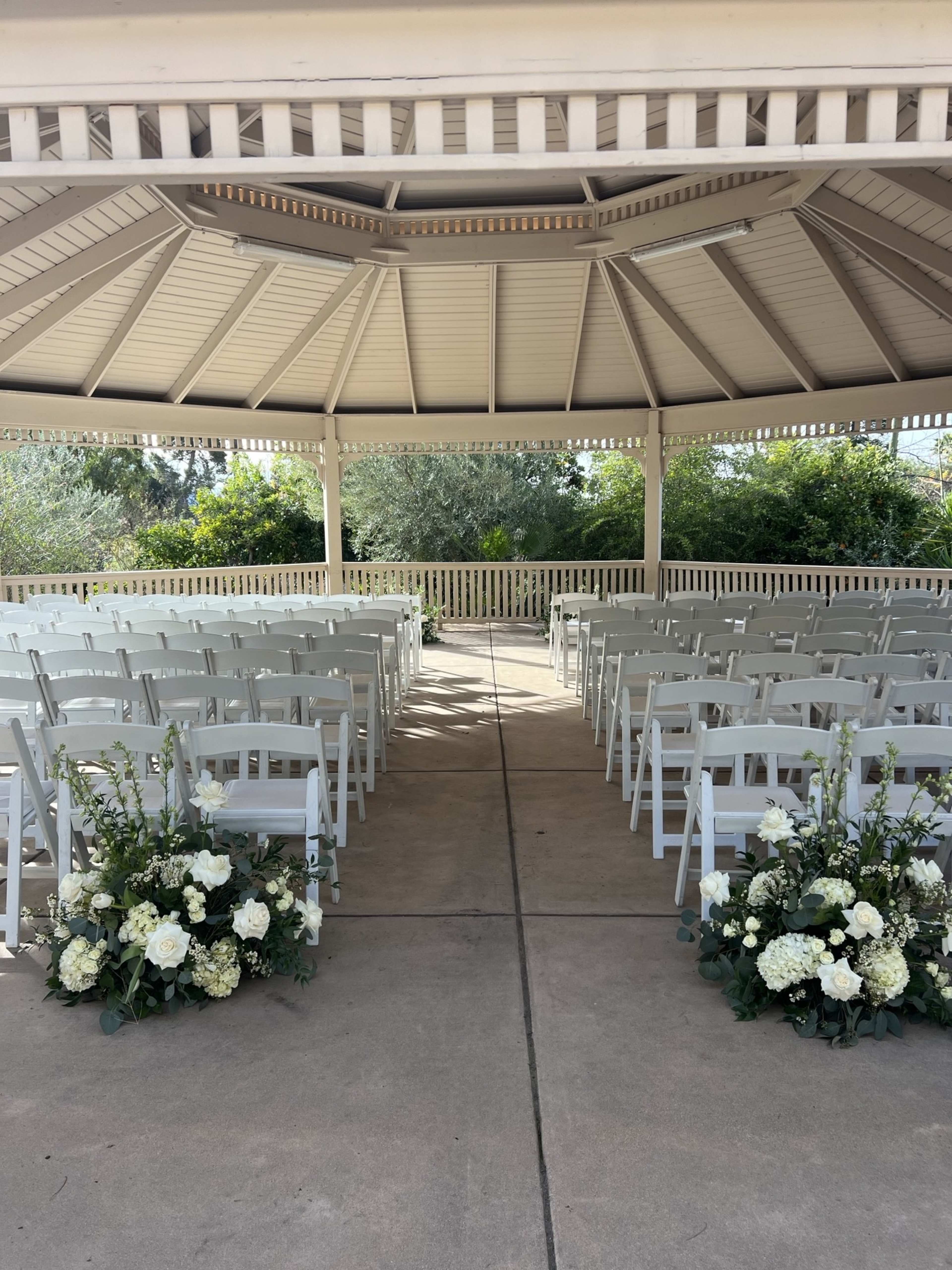 A gazebo with white chairs arranged in rows and floral arrangements positioned at the front.