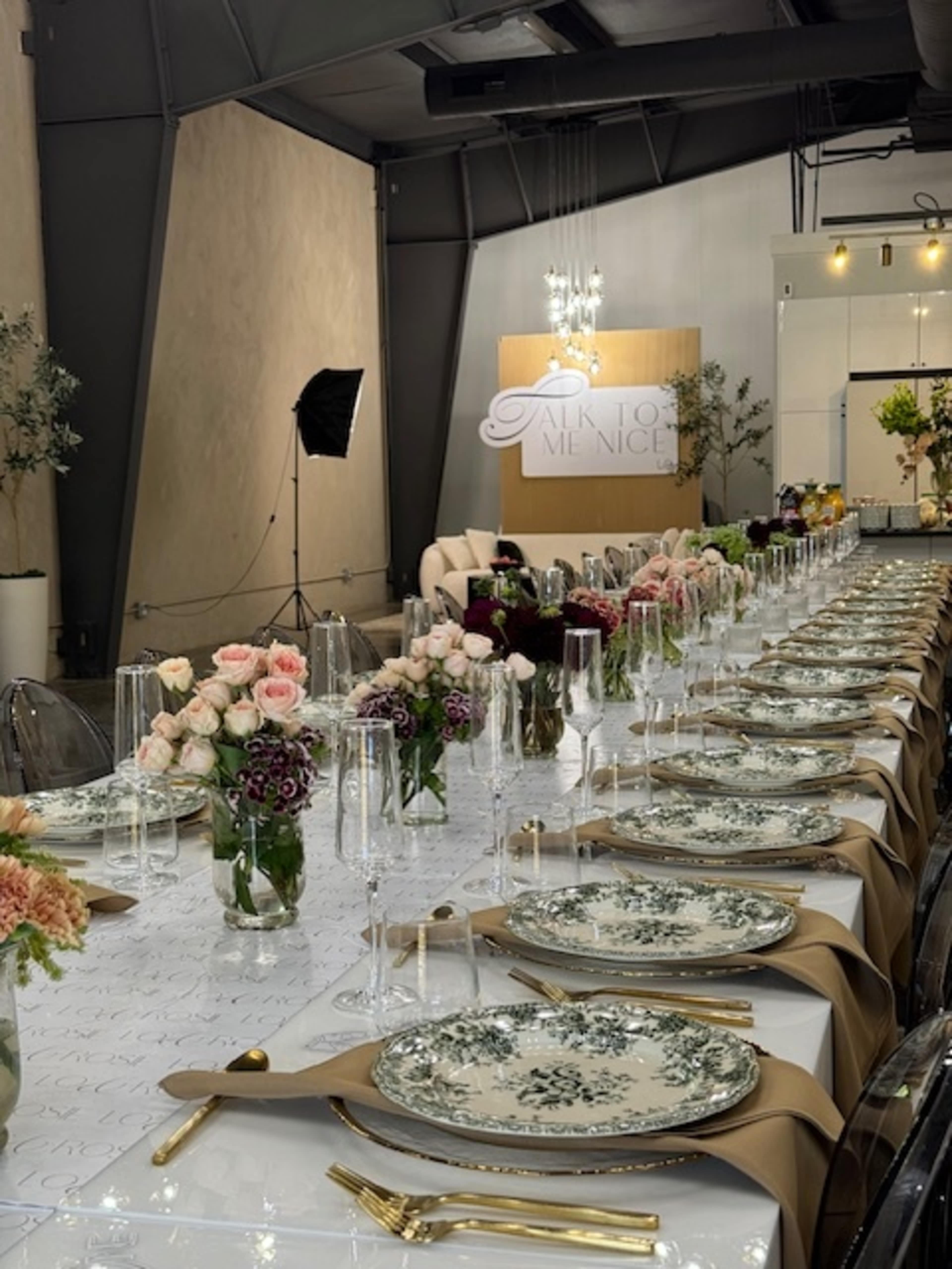 A long dining table is set with elegant dishes, floral centerpieces, and decorative glassware in a modern event space.