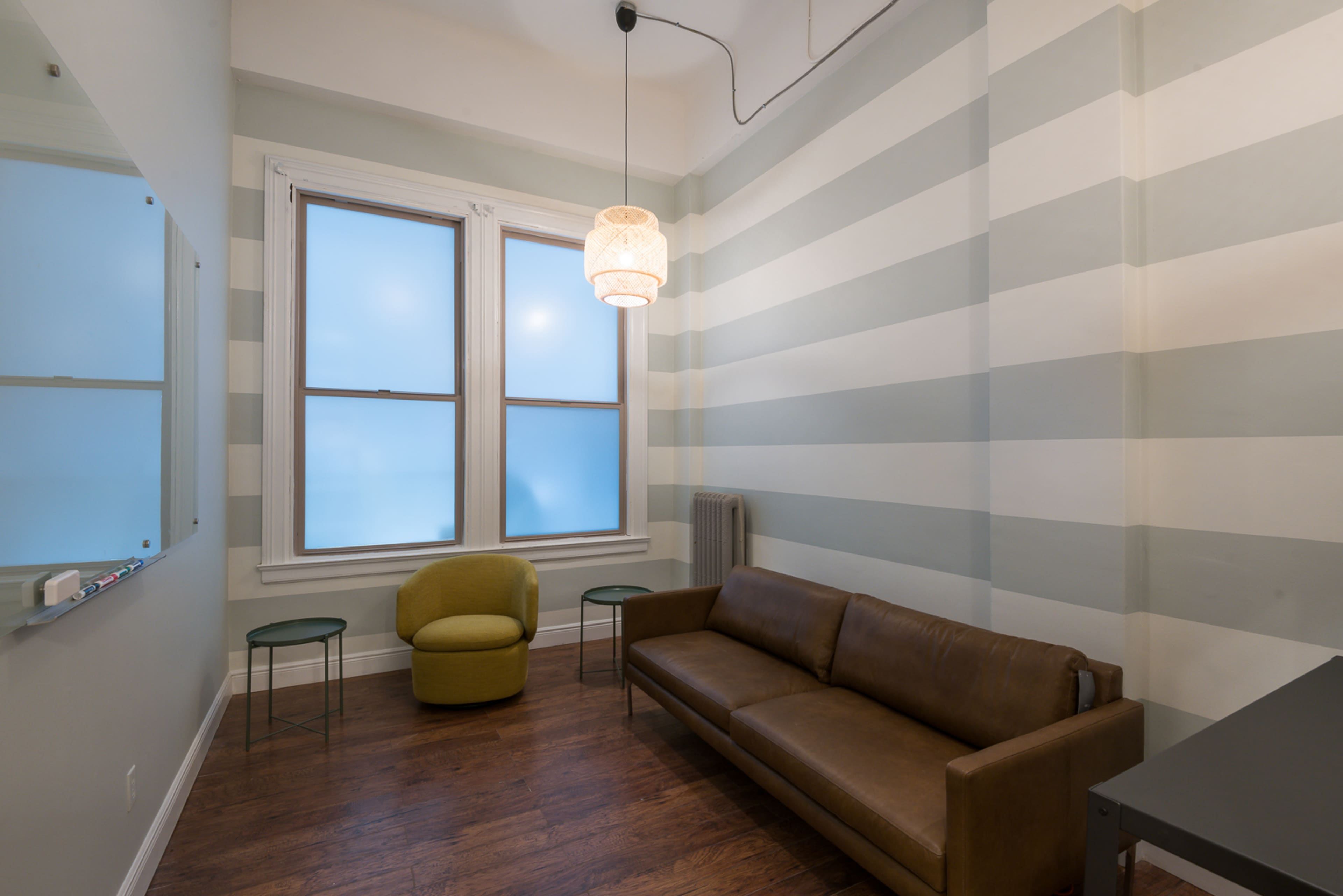 The room features a brown leather sofa and a green chair, with striped walls and two large windows.