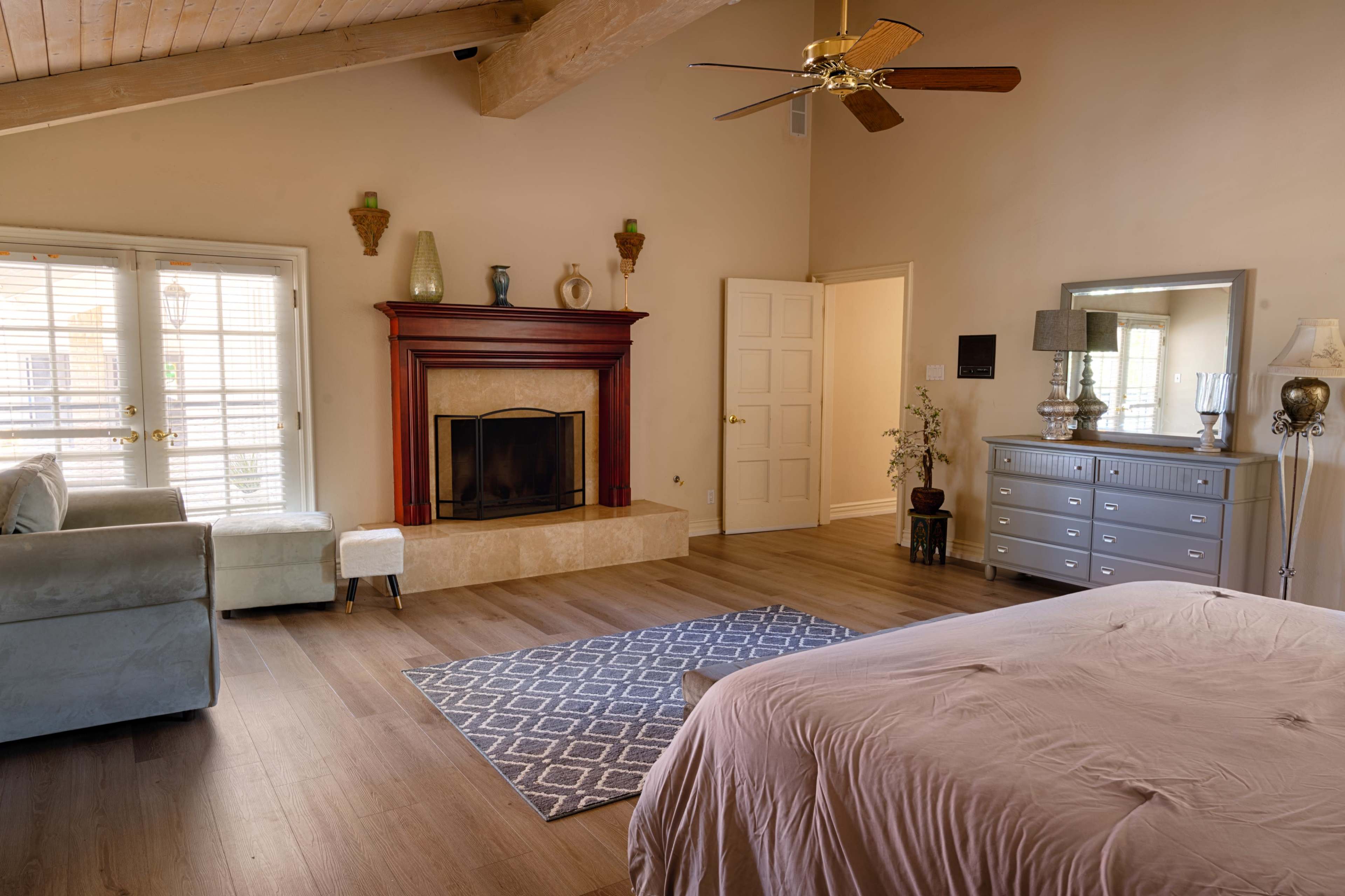 A spacious bedroom features a fireplace, a large mirror, a wooden dresser, and a seating area with a sofa.