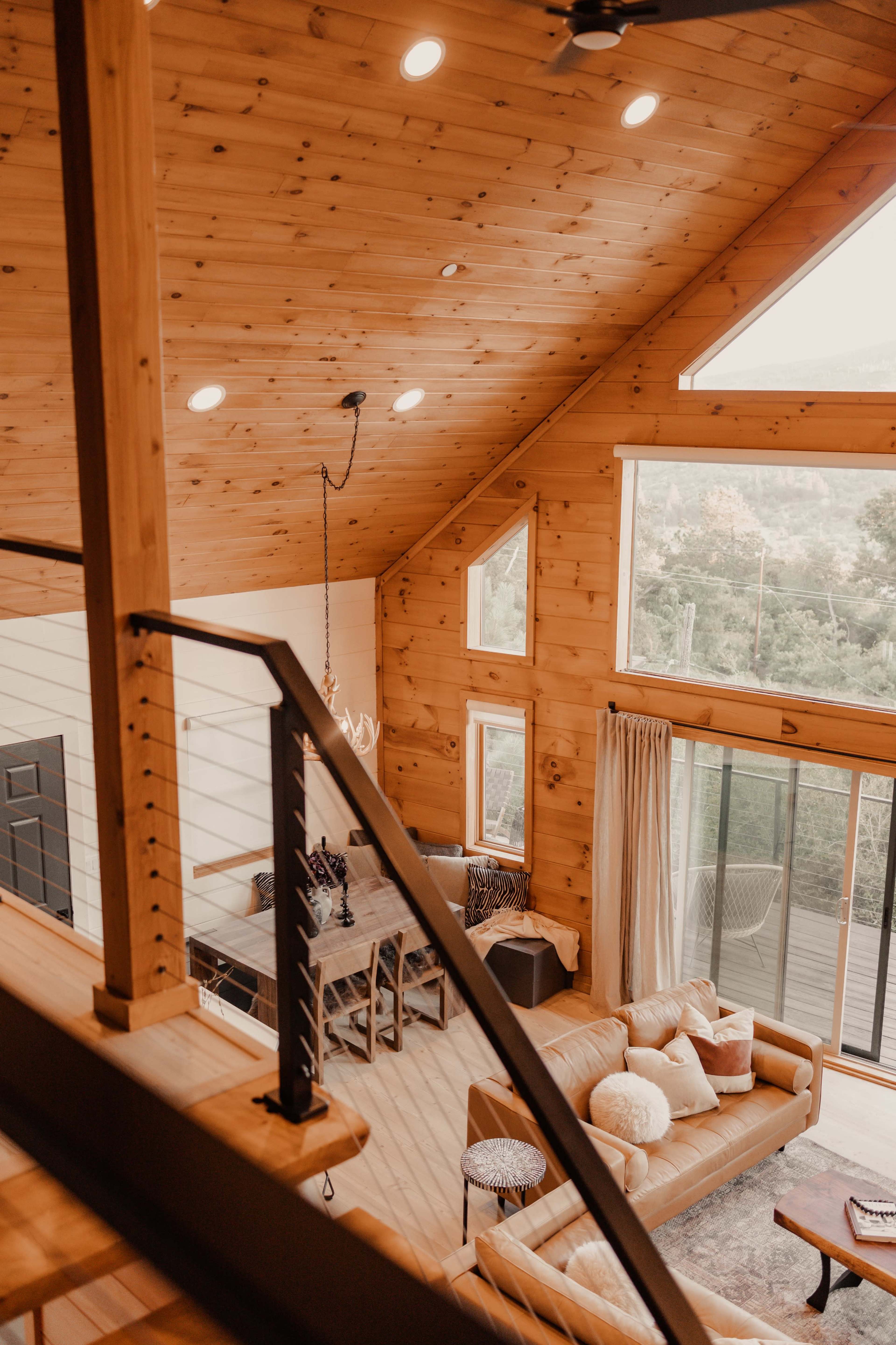 A large, open living area features wooden walls, a high ceiling with recessed lighting, and large windows overlooking a scenic view.