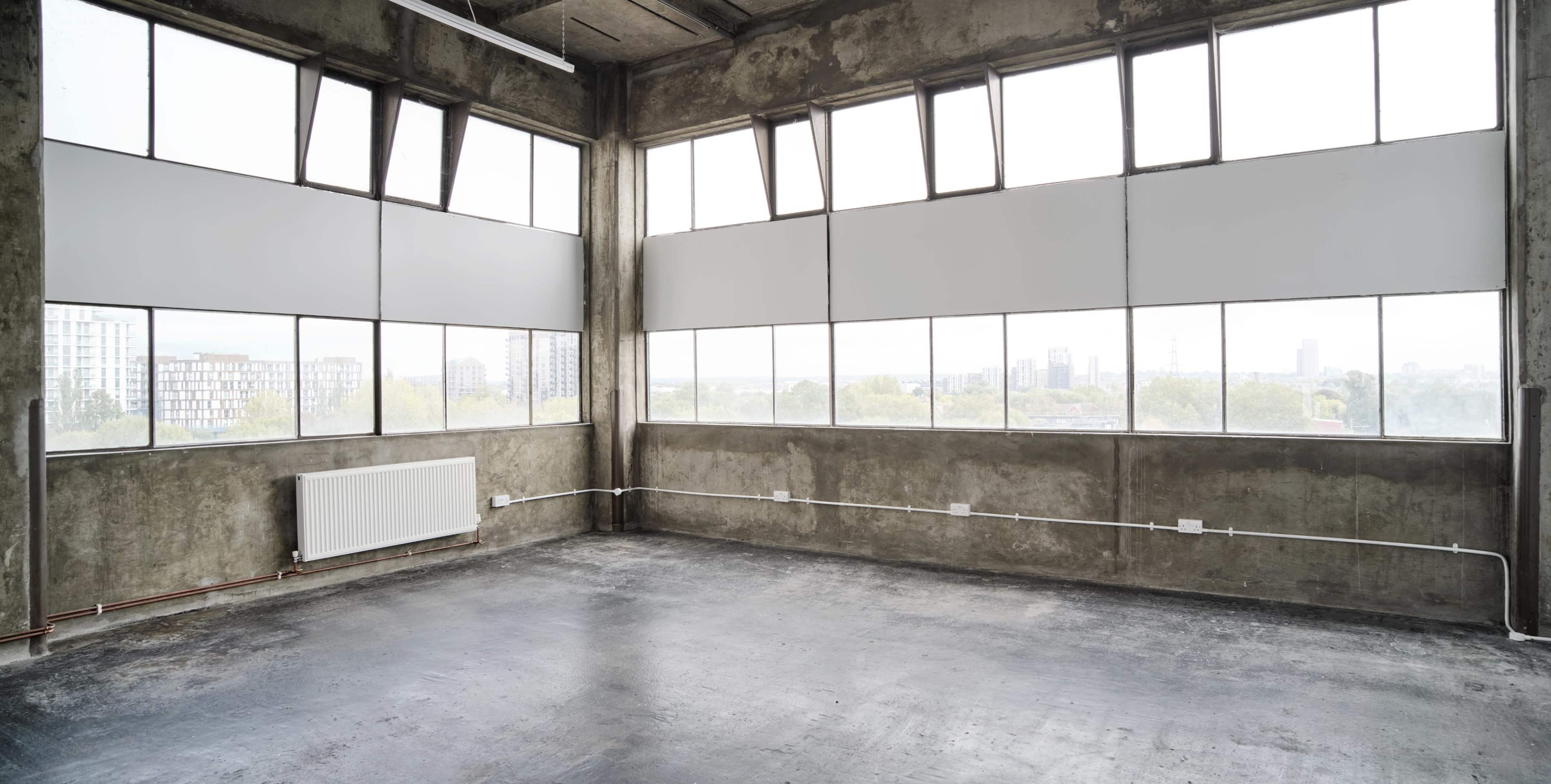 The image shows an empty industrial-style room with large windows and concrete walls.