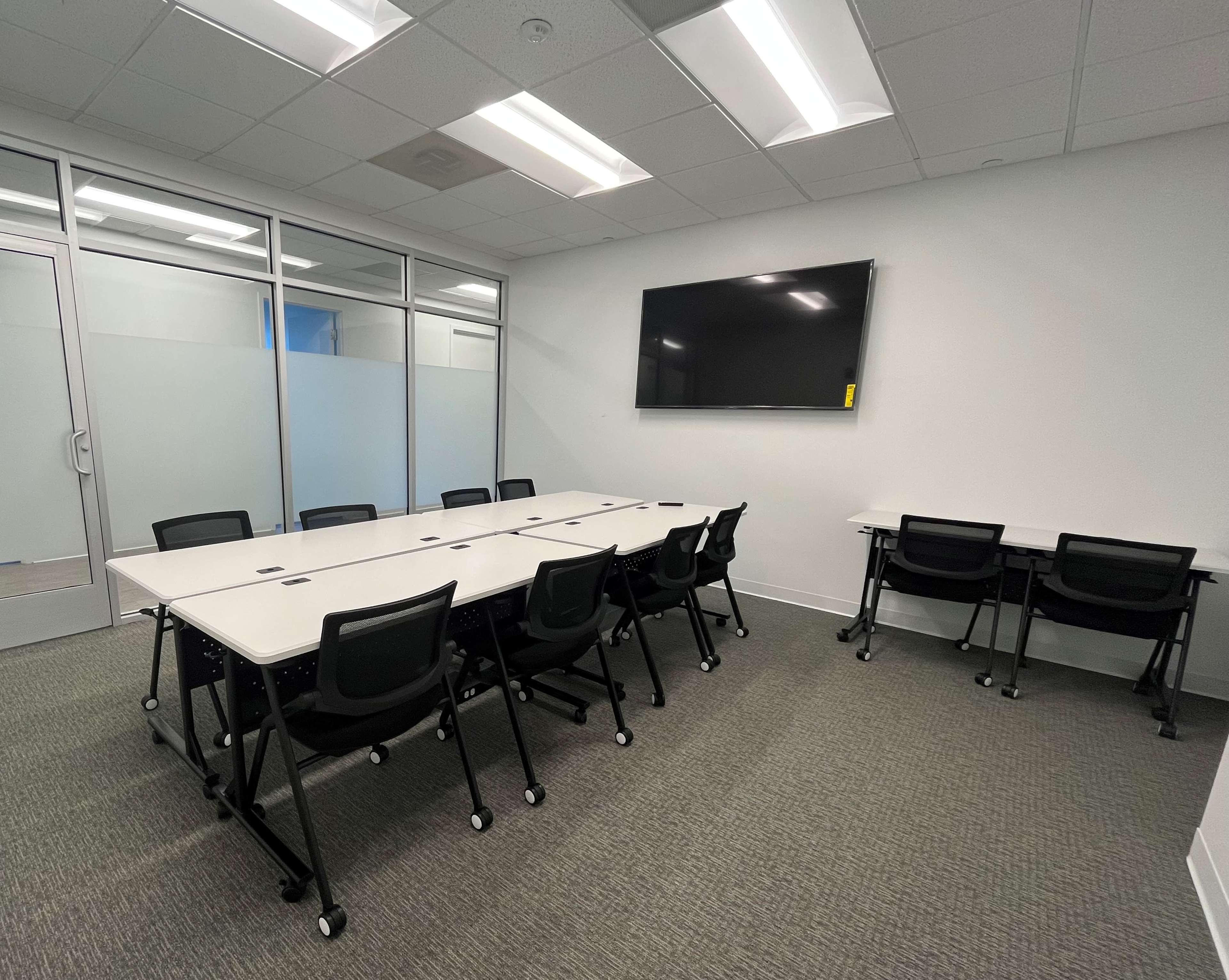A conference room with a large table surrounded by chairs and a wall-mounted TV.