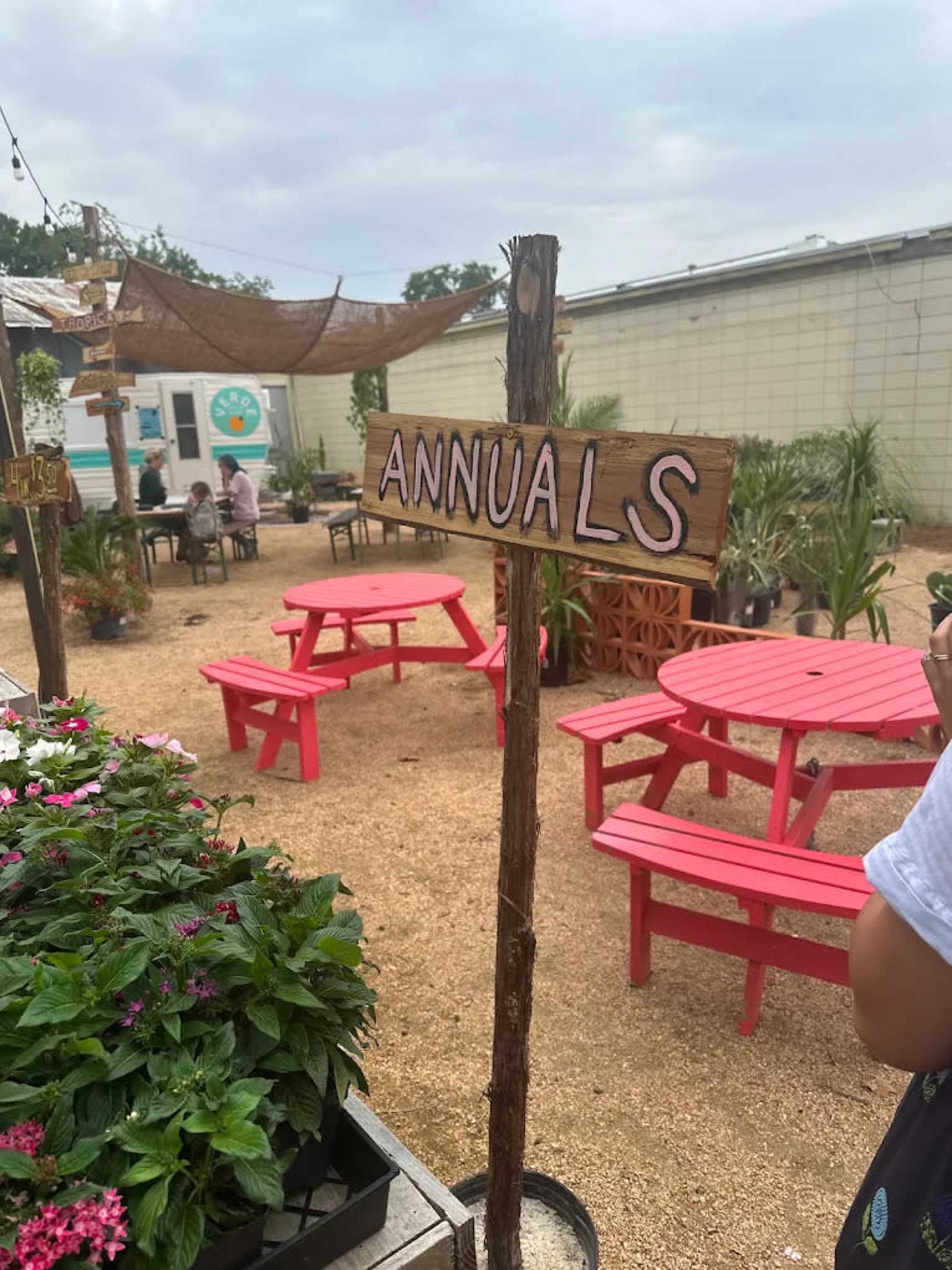 A wooden sign labeled "ANNUALS" stands in a garden area with pink picnic tables and various plants.