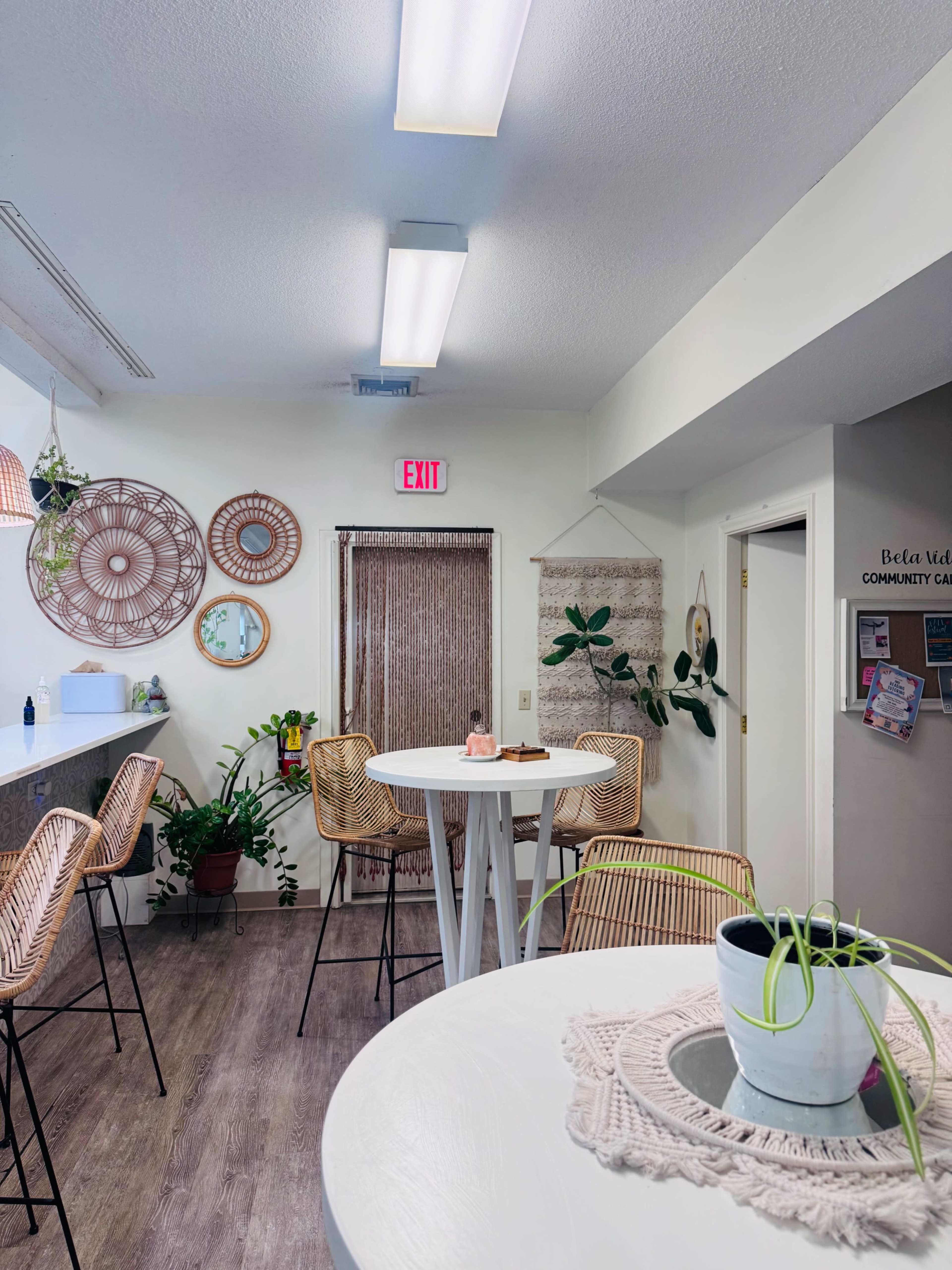 The image shows a bright, modern community space with woven decor, high chairs at a bar-style table, and plants enhancing the ambiance.