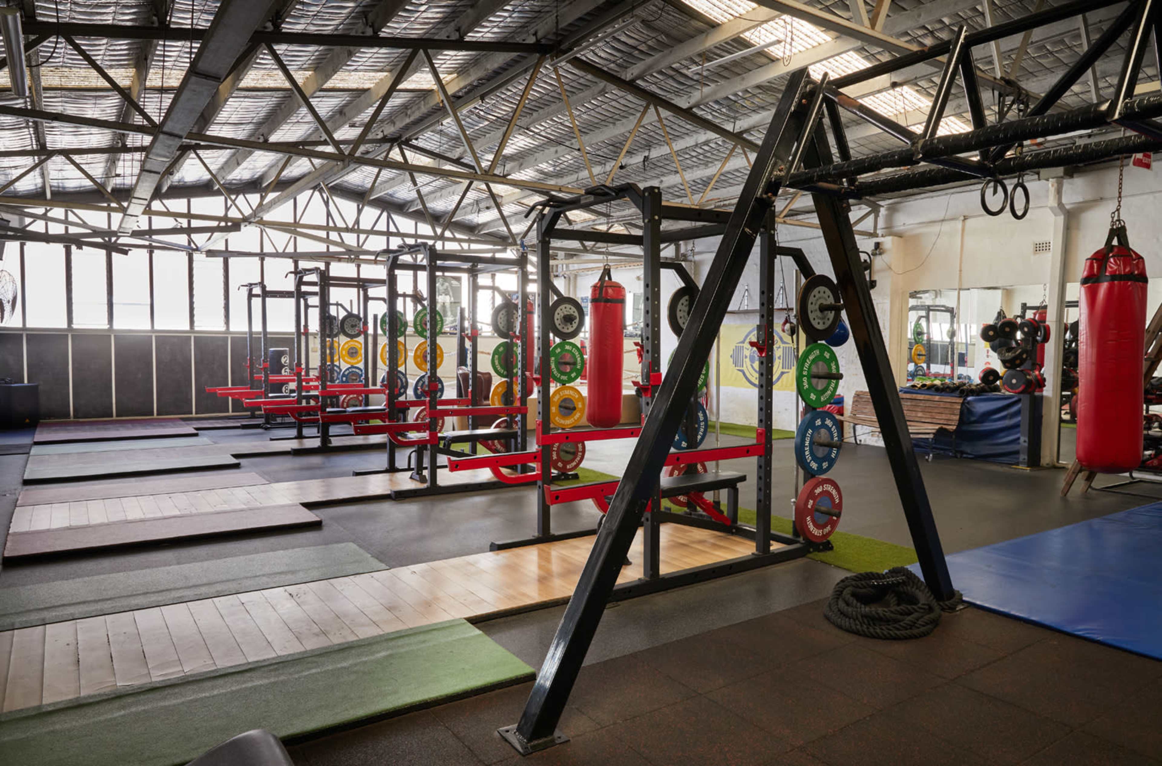 An interior view of a gym featuring weightlifting equipment, punching bags, and a variety of exercise surfaces.