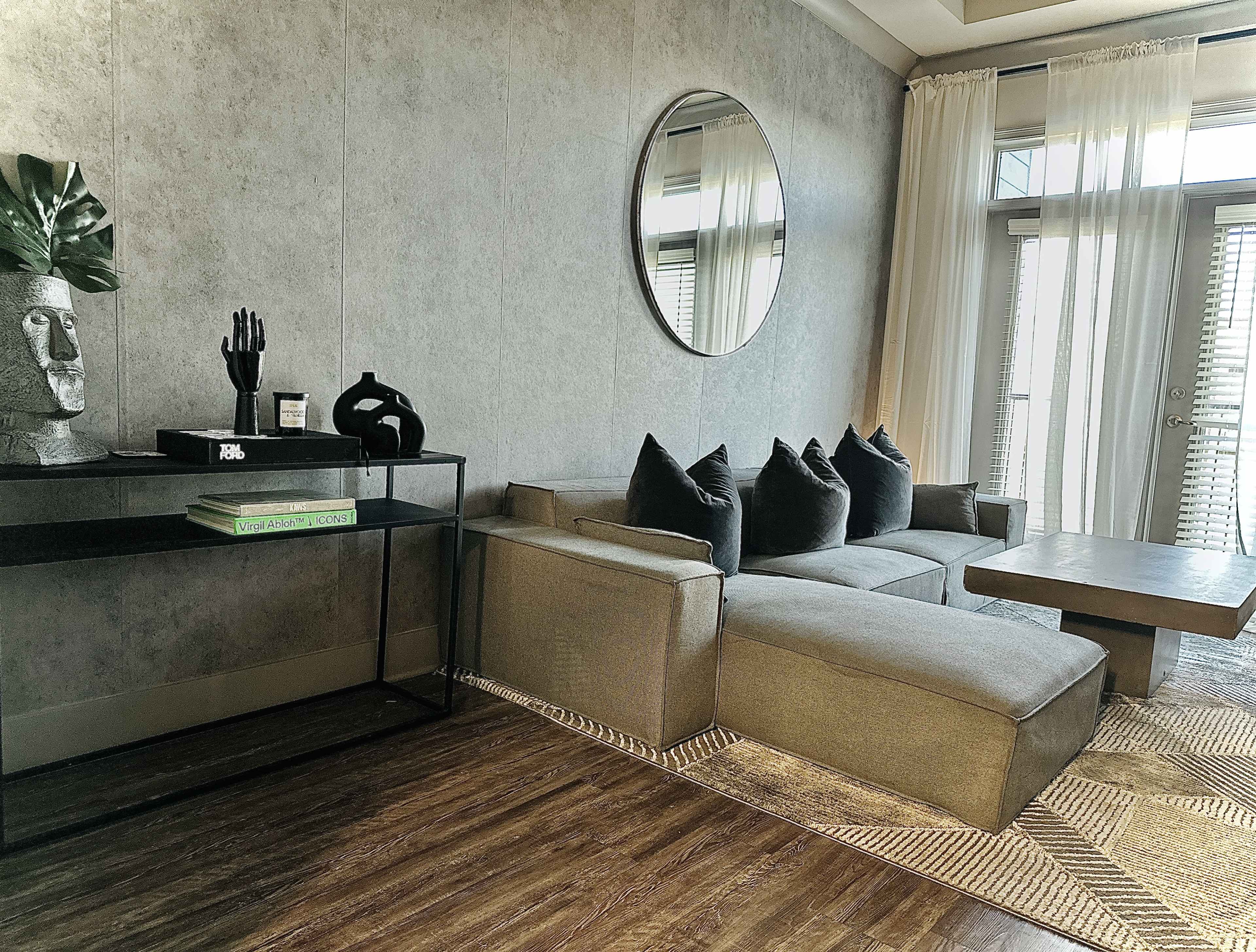A modern living room with a sectional sofa, a round mirror on the wall, a coffee table, and decorative elements including a plant and sculptures.
