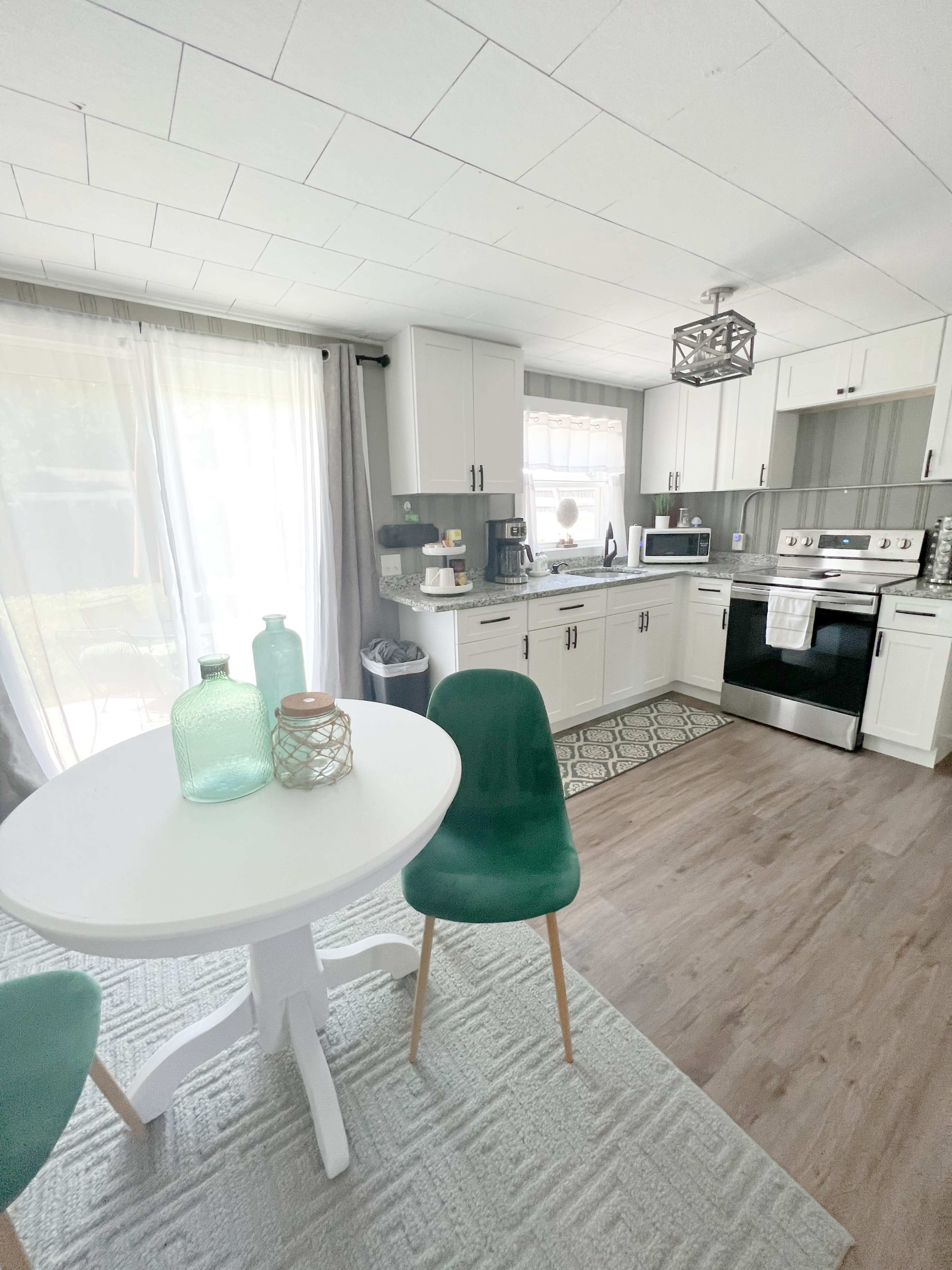 A bright kitchen features white cabinets, a black stove, and a round dining table with green chairs.