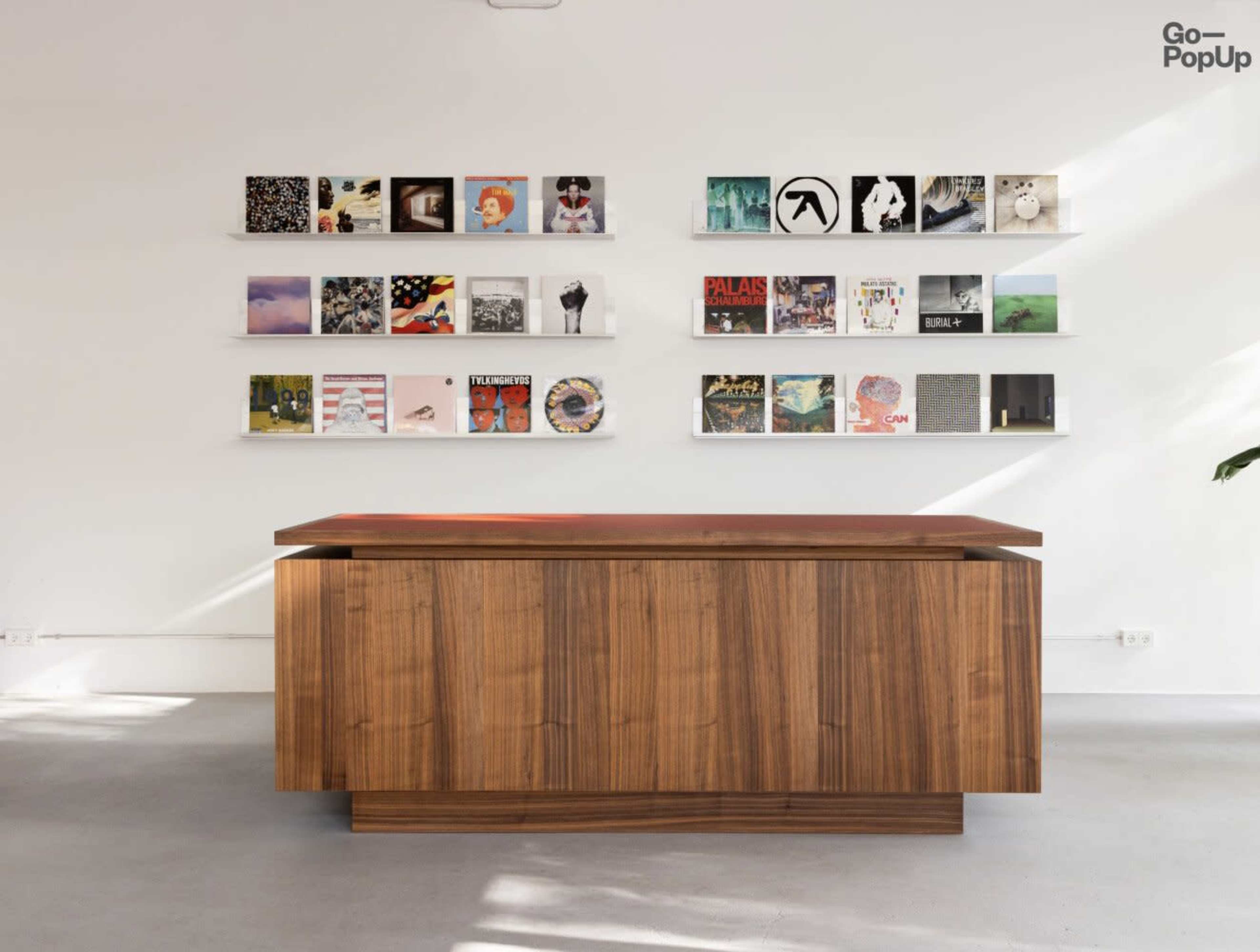 A wooden counter stands in front of a wall displaying various album covers arranged in a grid format.
