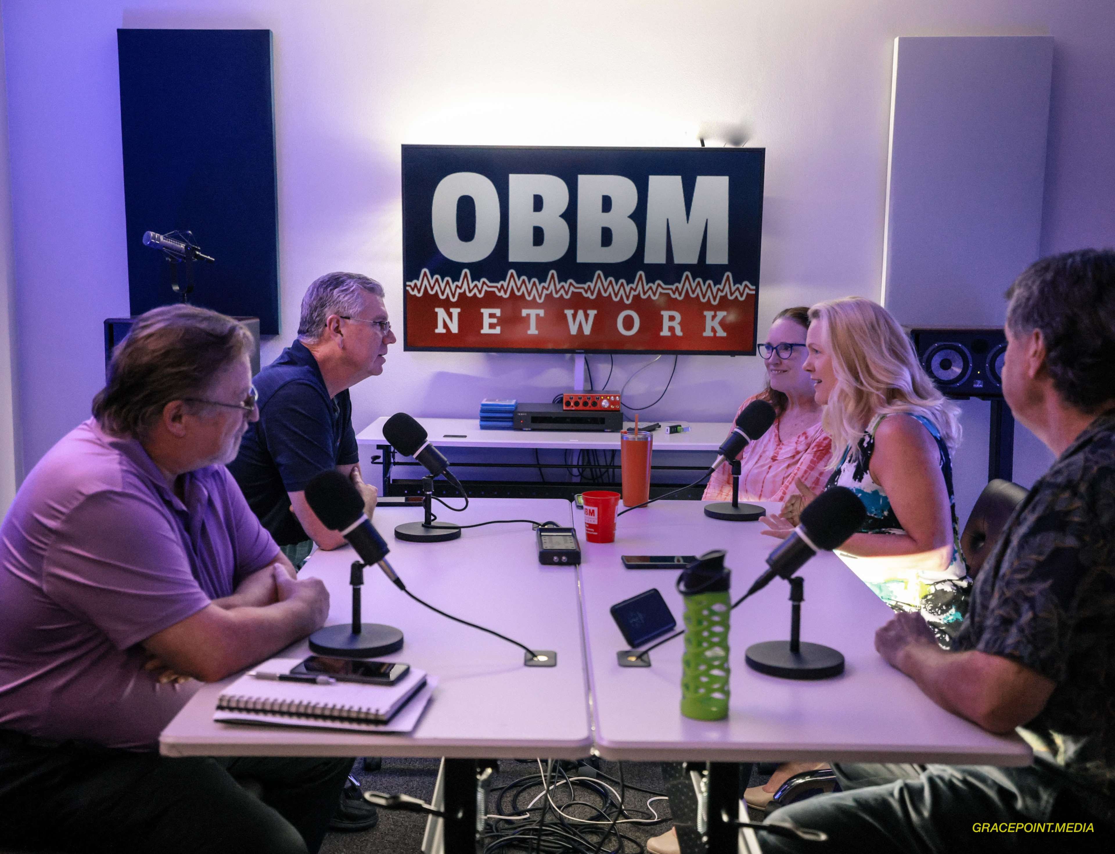 A group of five individuals participates in a discussion at a podcast studio featuring the "OBBM Network" sign on the wall.