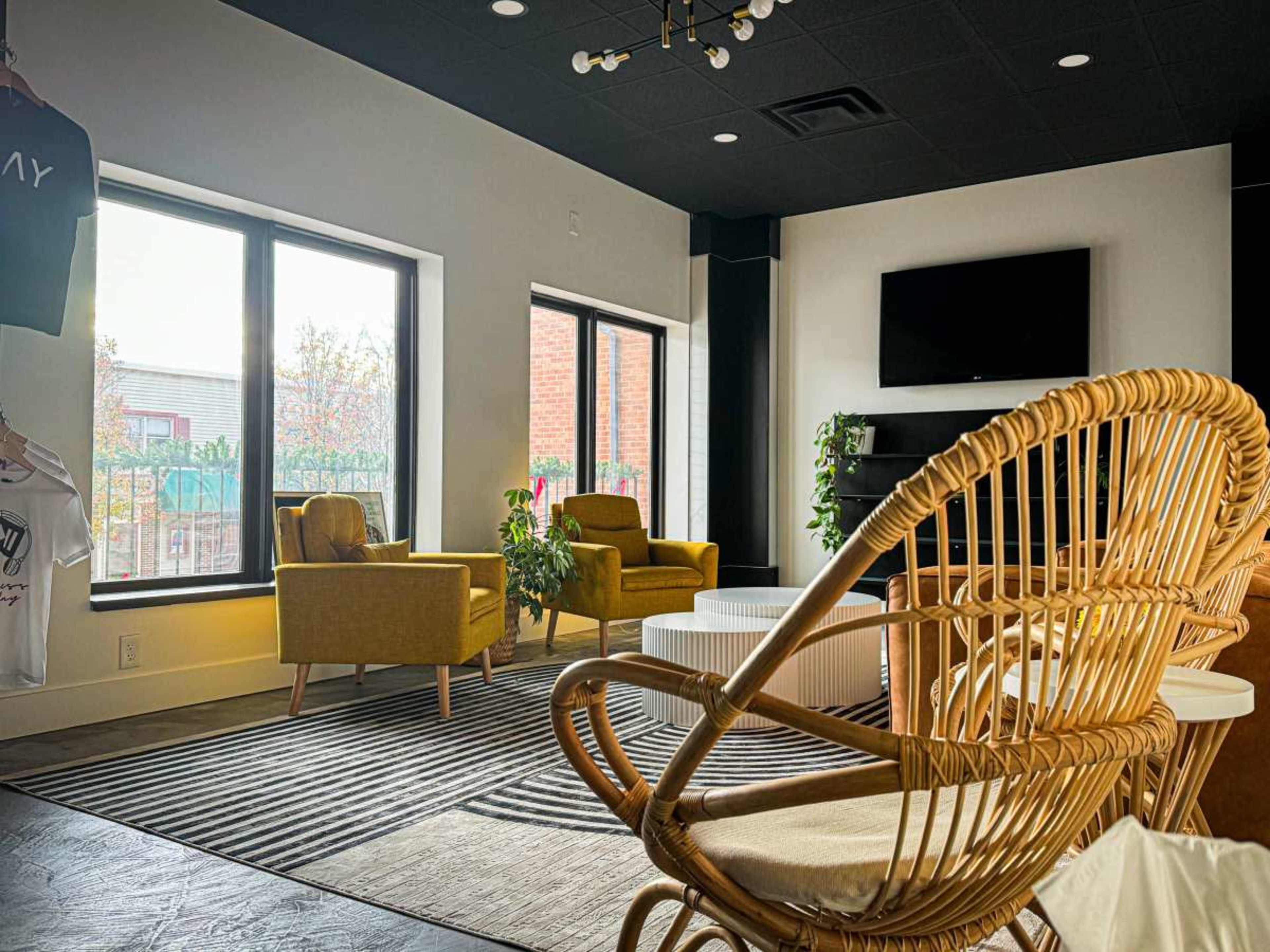 A modern, well-lit lounge area with two yellow chairs, a round white coffee table, and large windows overlooking greenery.