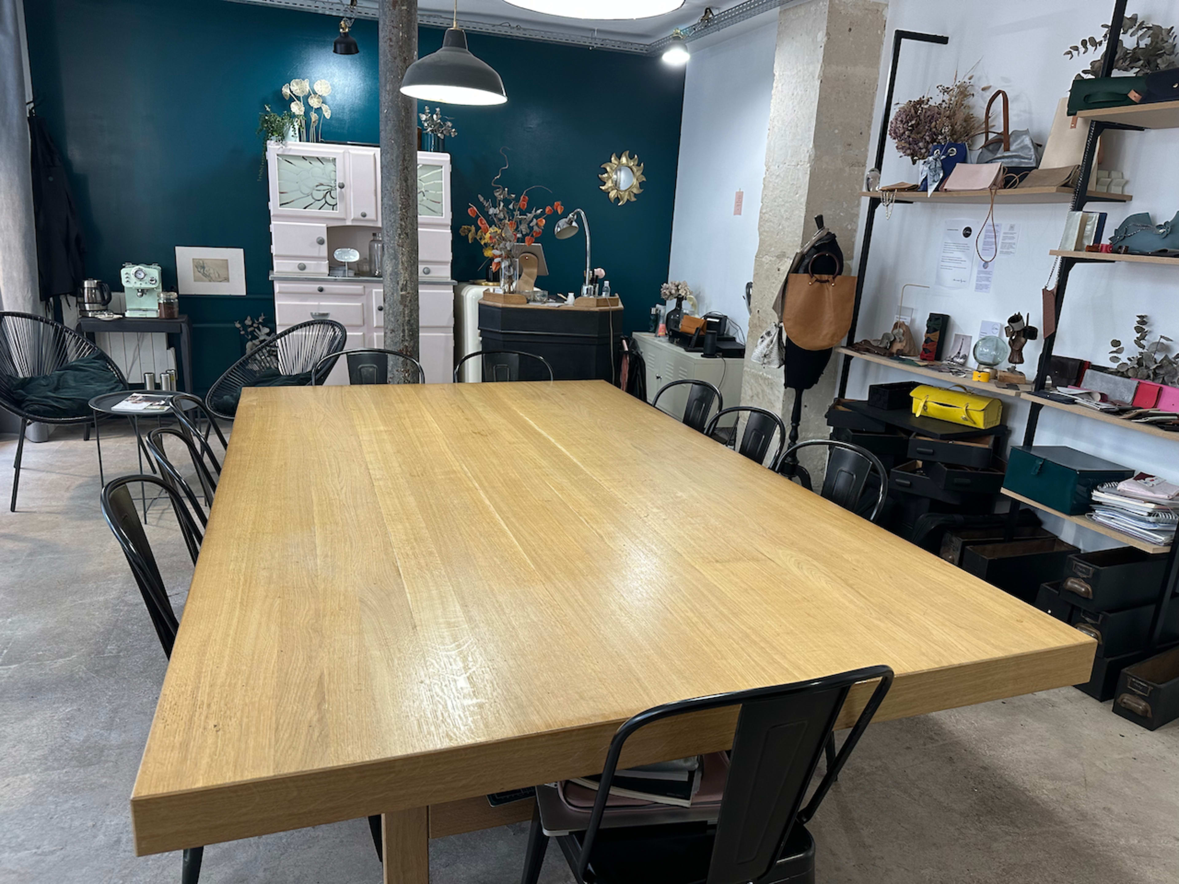 A large wooden table surrounded by black chairs in a well-decorated workspace with a green accent wall and various items on shelves.