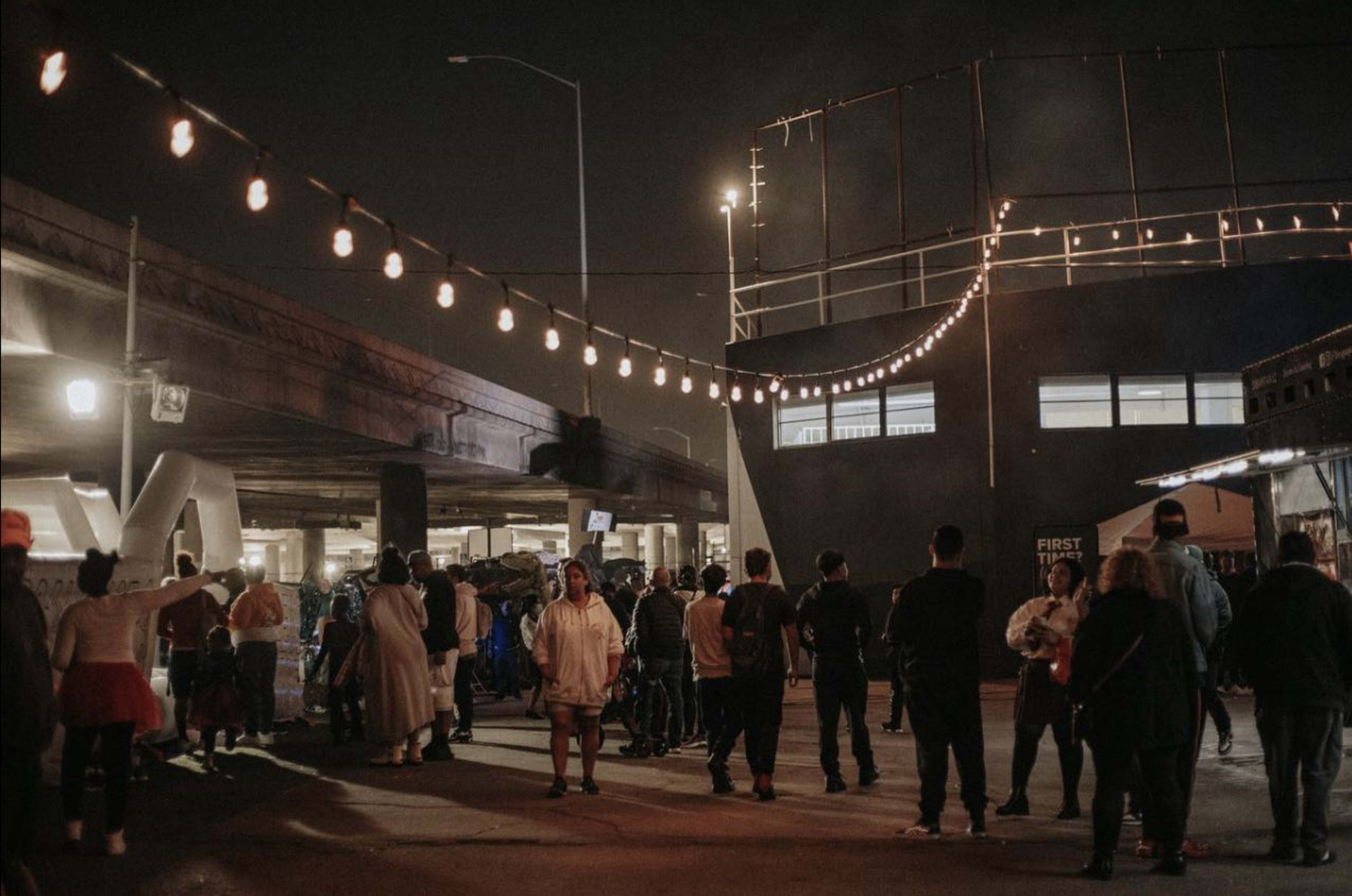 A crowd gathers under string lights near a building at night.