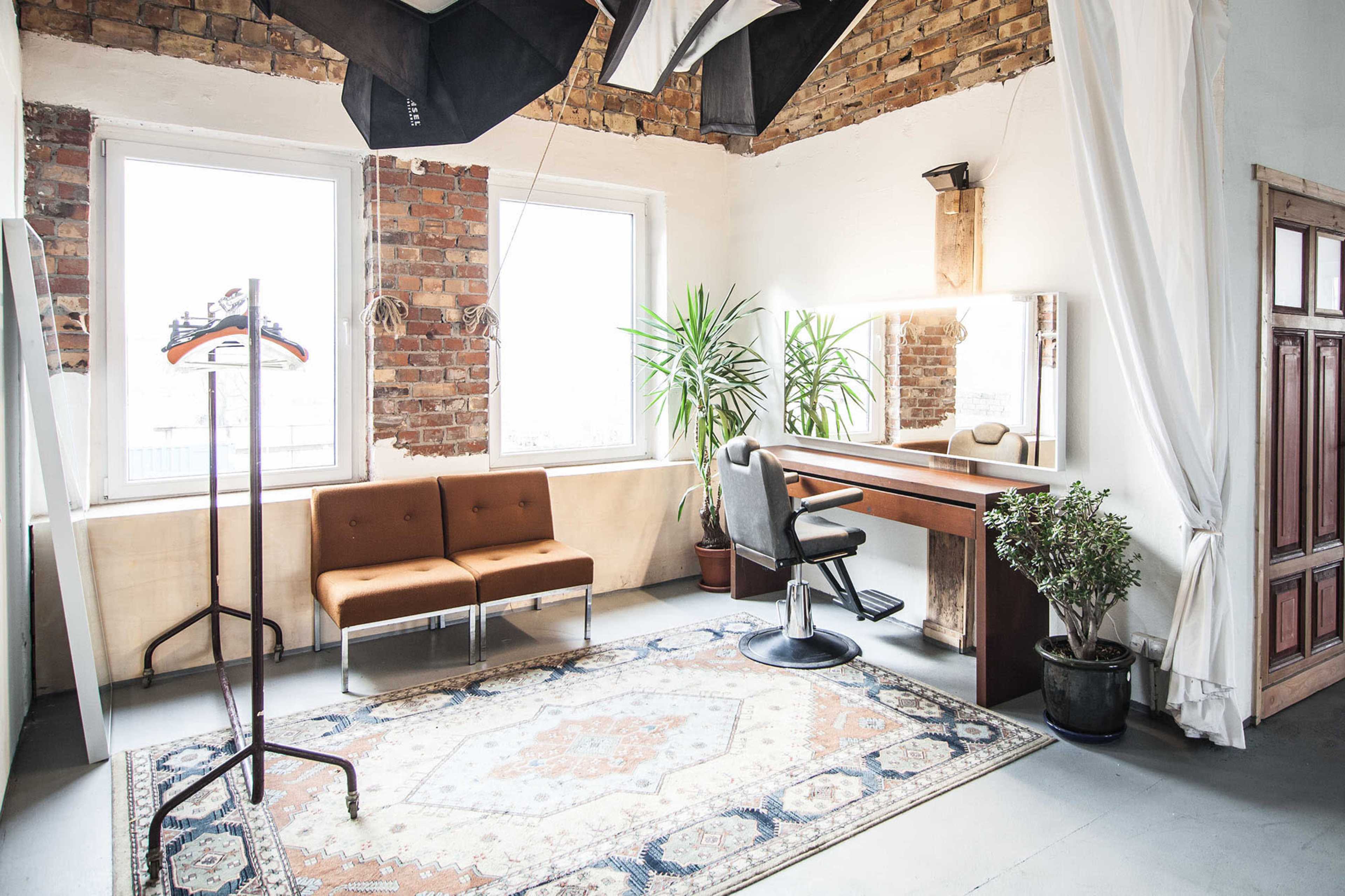 A brightly lit room featuring a makeup station, an orange seating area, and a large plant alongside a patterned rug.