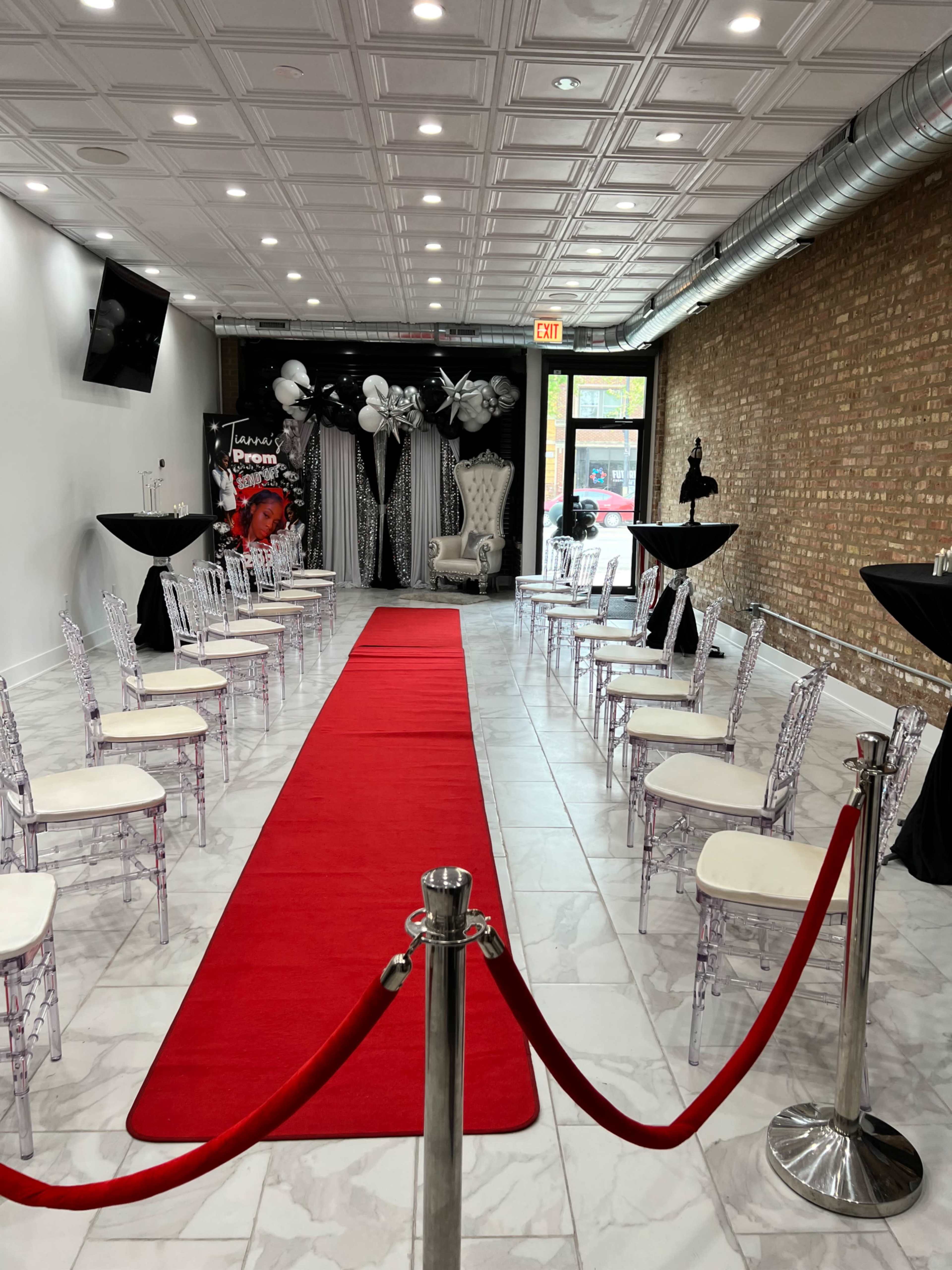 A room set up for an event, featuring a red carpet leading to a decorated backdrop, with chairs arranged on either side.