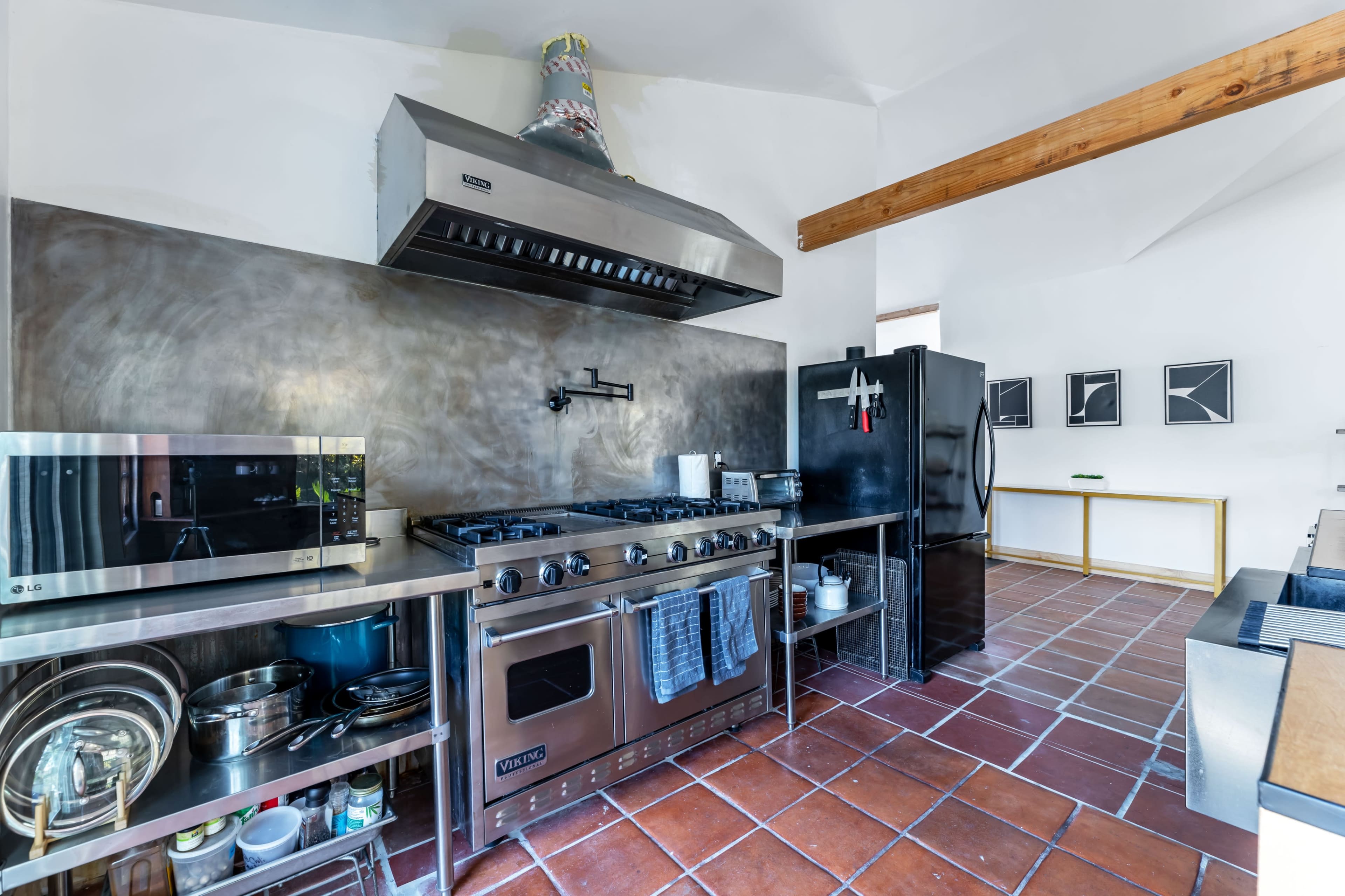 The kitchen features stainless steel appliances, a large gas stove with an overhead hood, and a tiled floor.