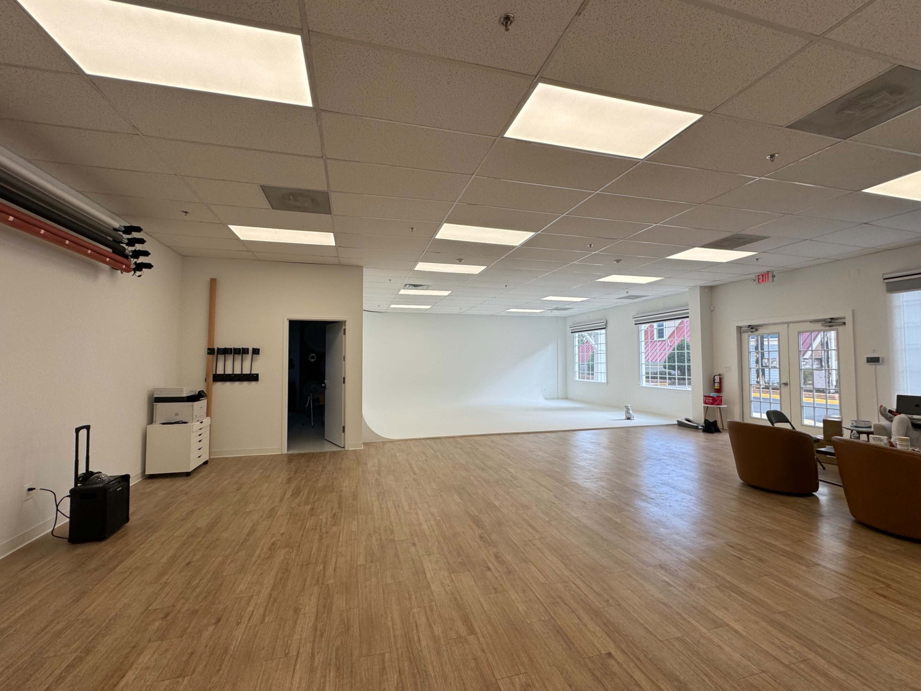 A spacious, well-lit studio with wooden flooring, a seamless backdrop on one wall, and various furniture along with a small workstation.