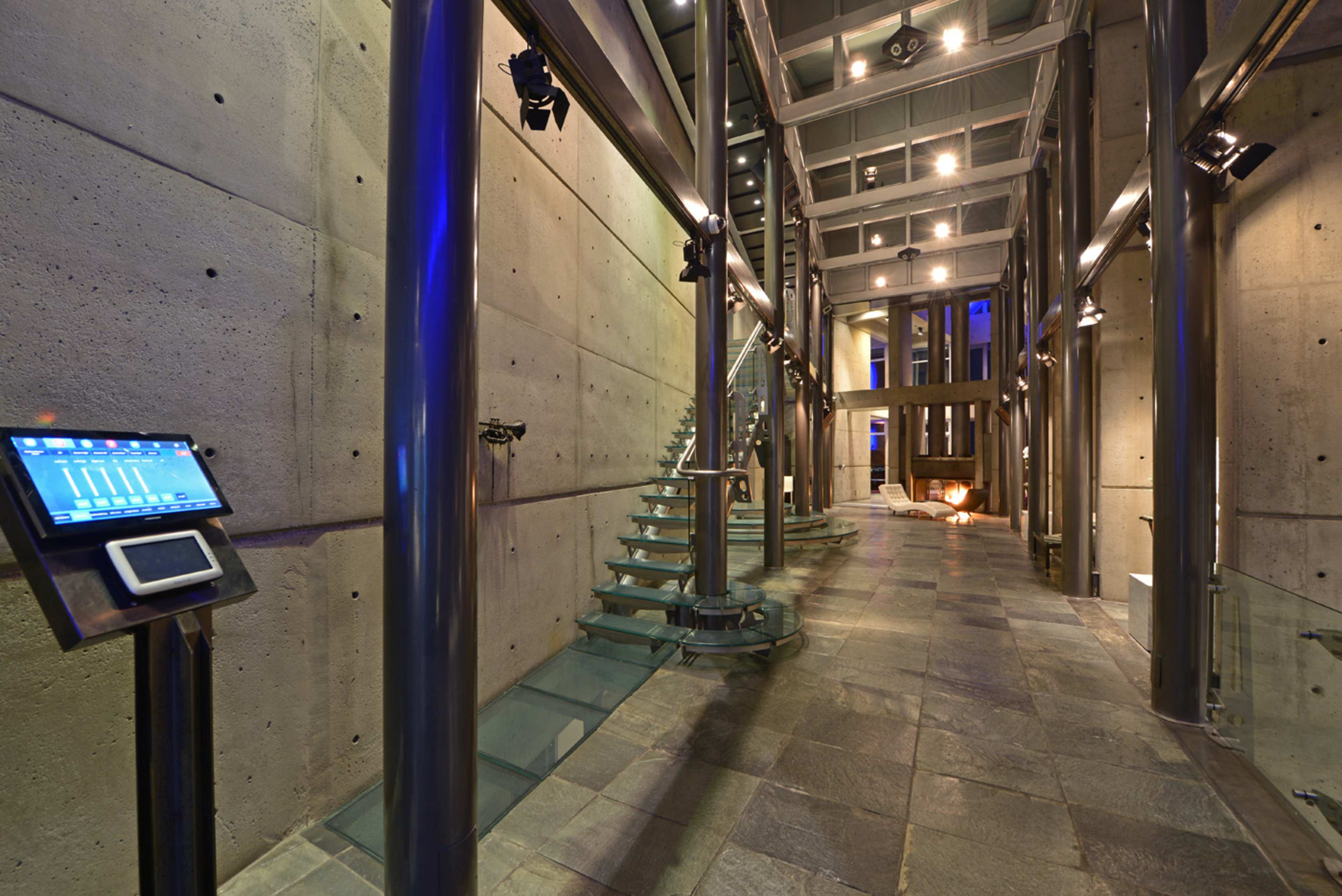 A modern interior space with an open staircase, glass railings, and concrete walls, illuminated by overhead lights.
