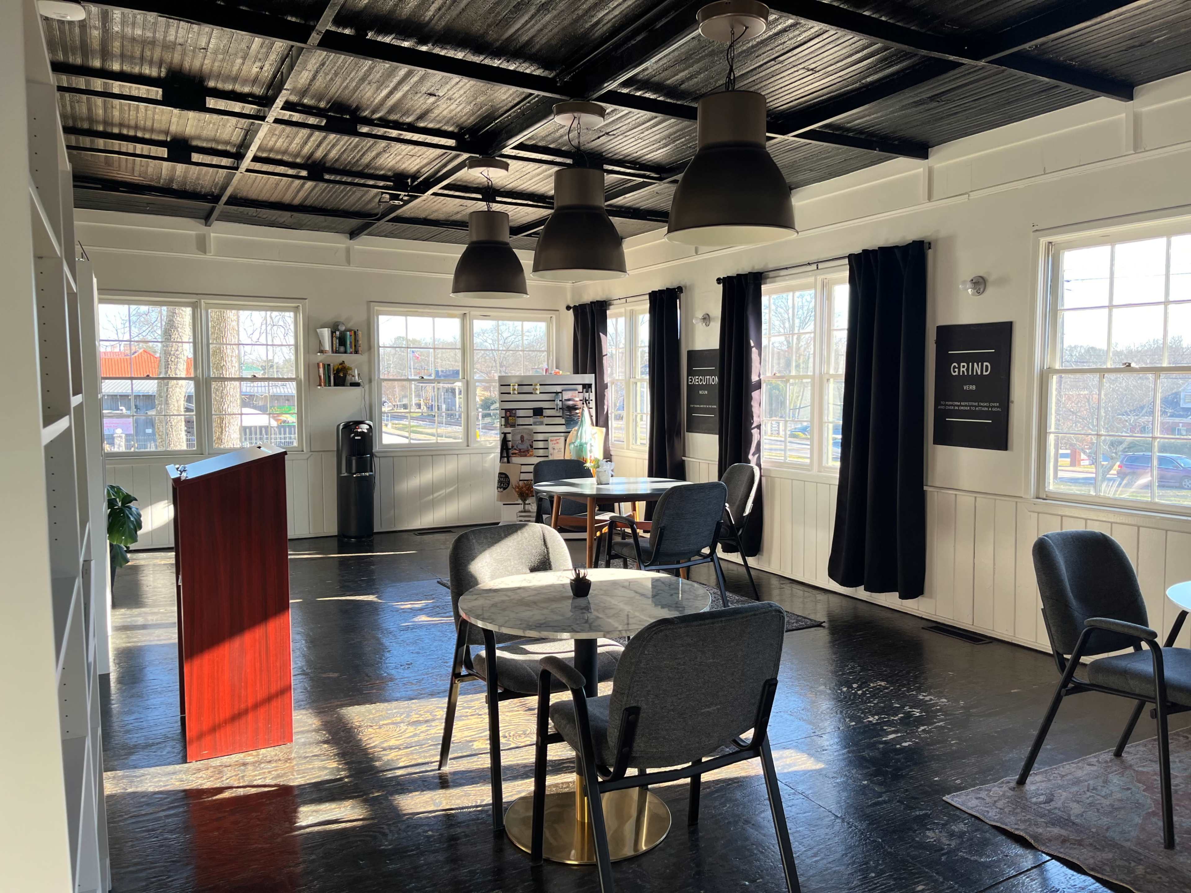 A well-lit, modern co-working space with tables, chairs, and large windows.
