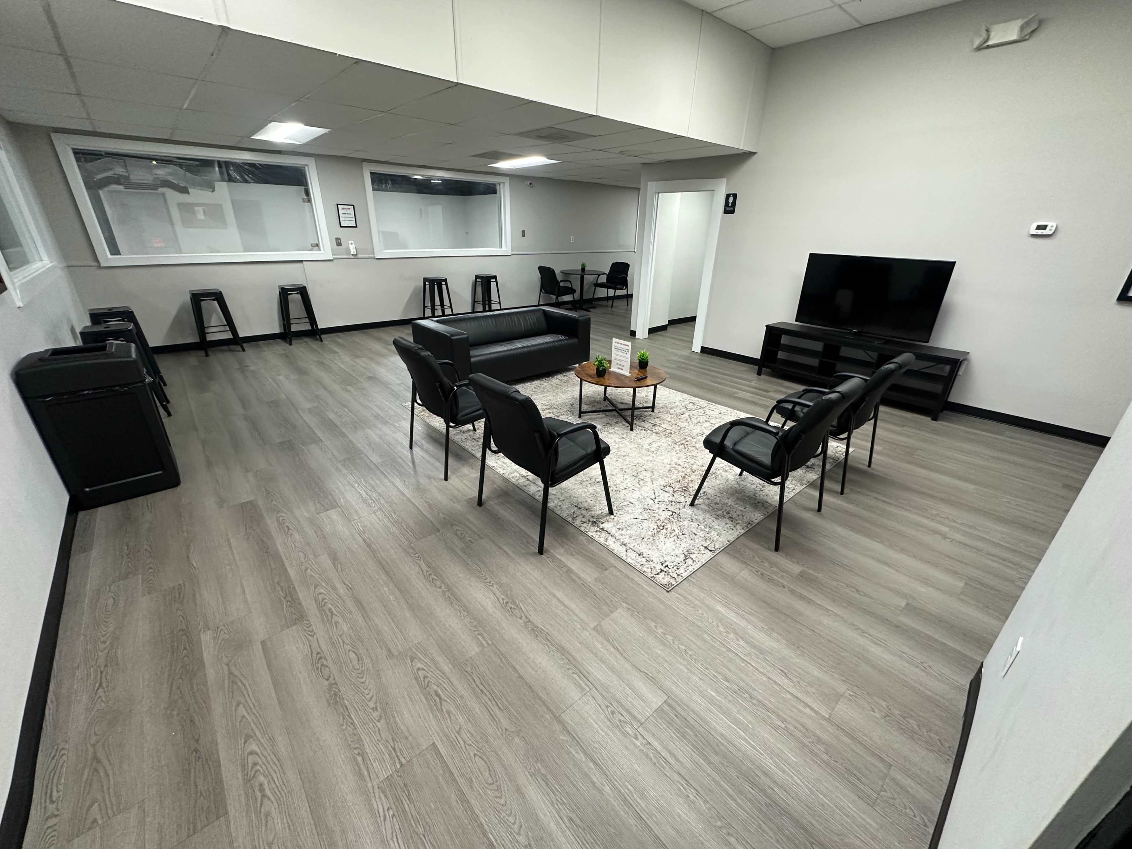 A modern waiting room features a couch, several black chairs, a coffee table, a television, and a light rug on a hardwood floor.