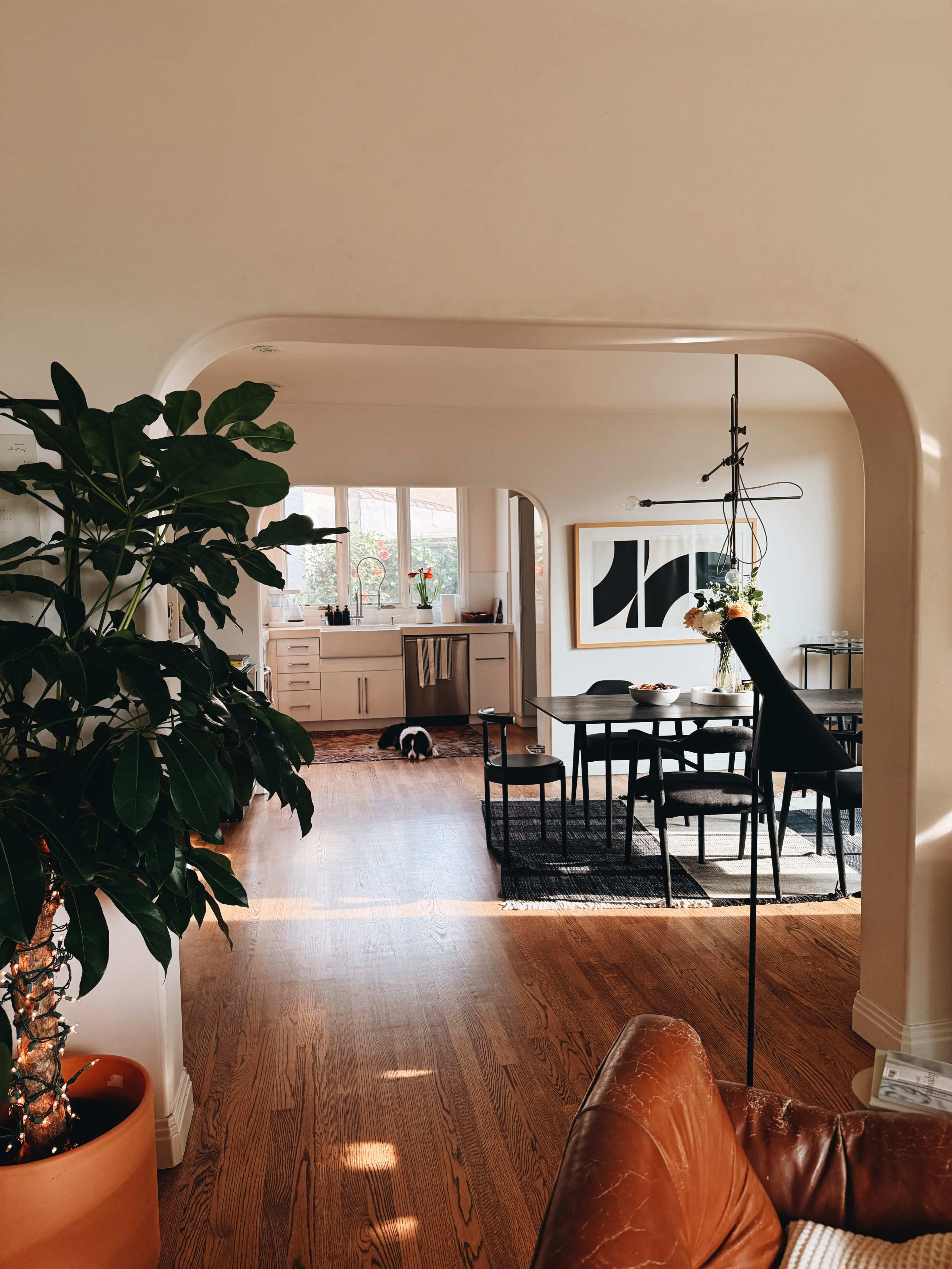 A cozy living area features an archway leading to a dining space with a table and chairs, illuminated by natural light.