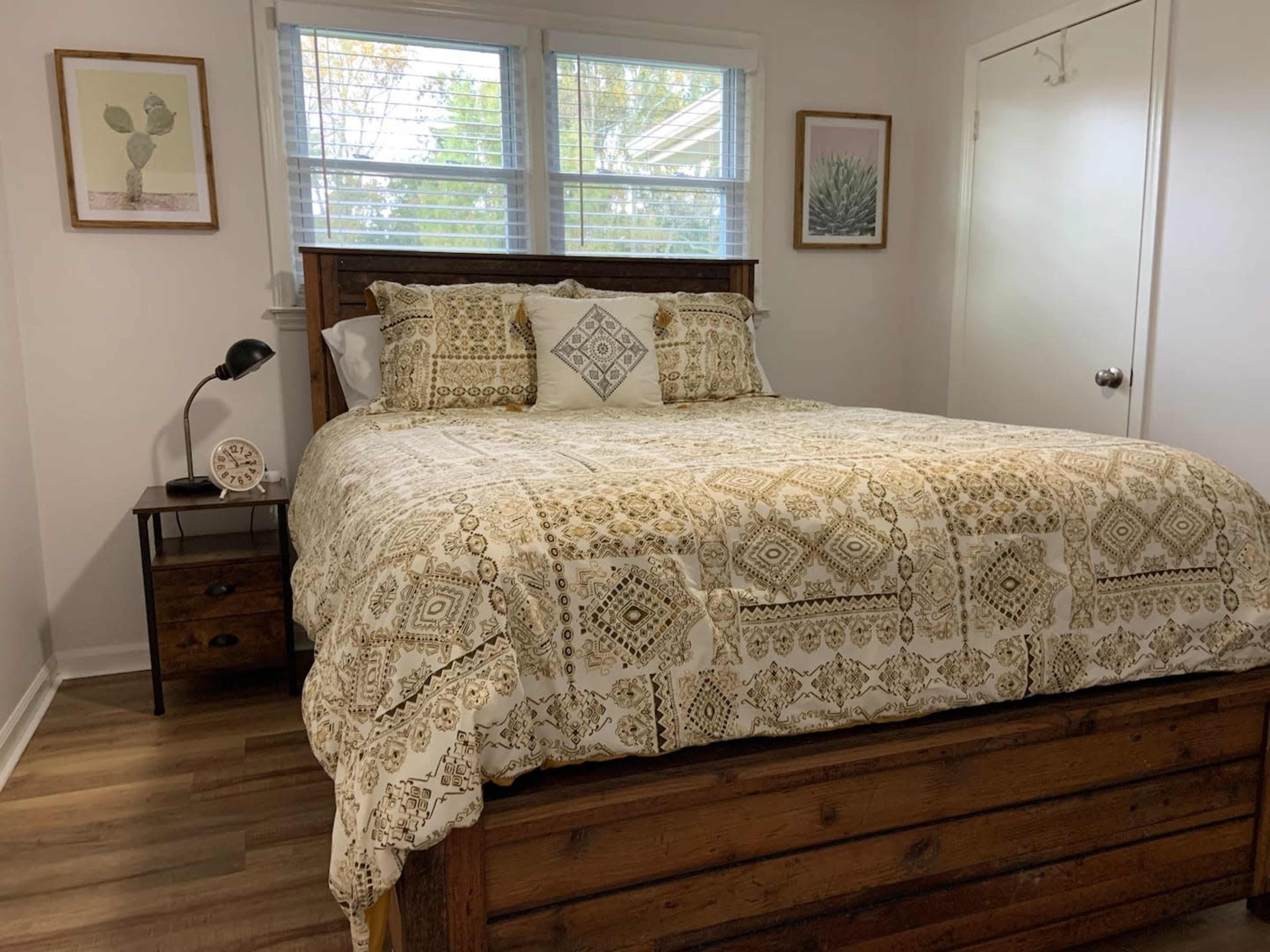 A neatly made bed with a patterned comforter in a well-lit bedroom featuring a nightstand and a window.