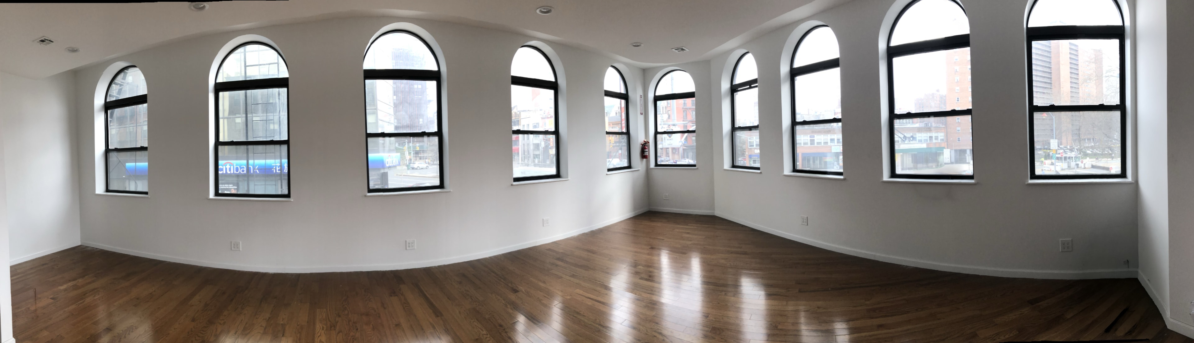 The image shows a panoramic view of a room with multiple arched windows and hardwood floors.