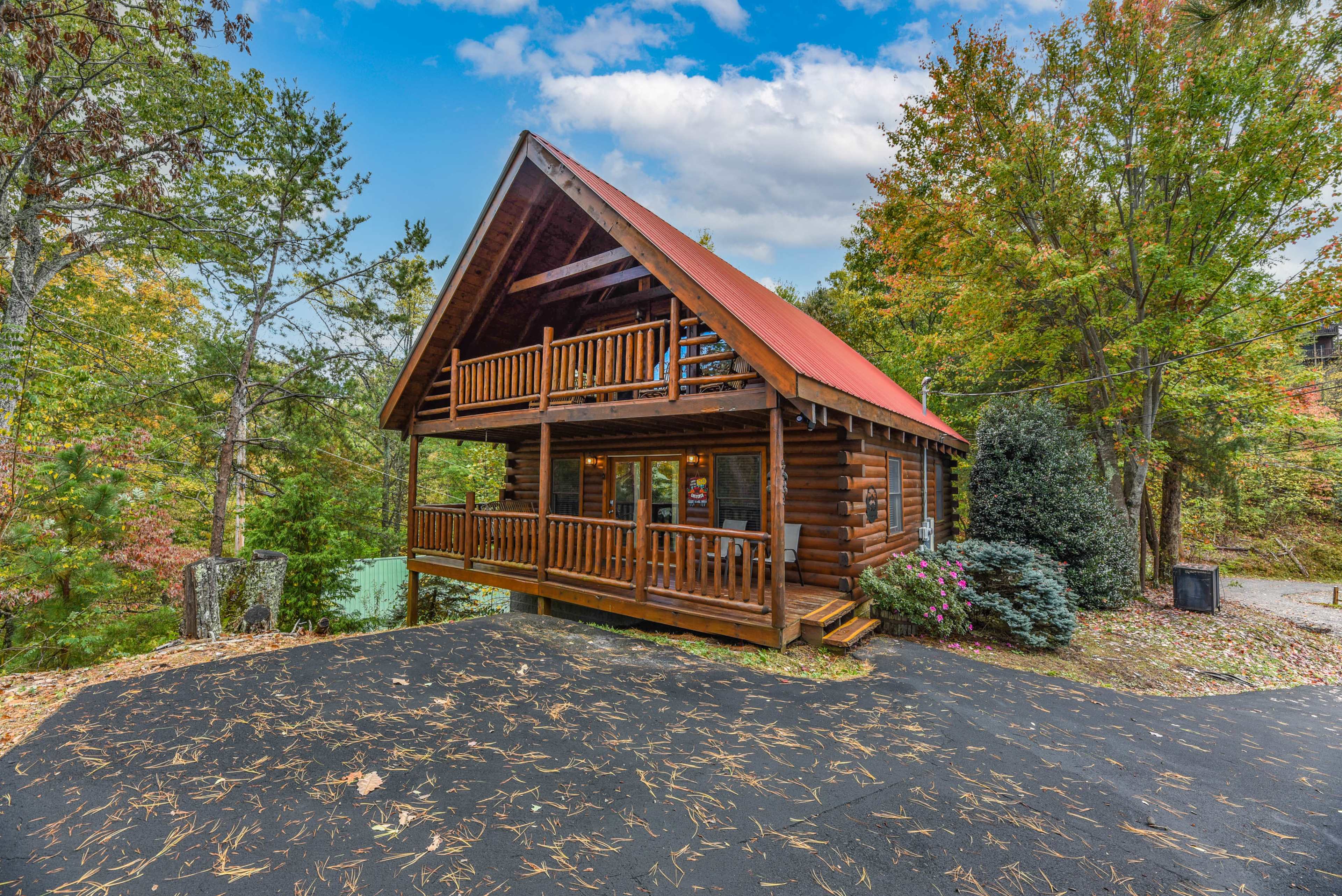 A wooden cabin with a sloped roof, adorned with balconies, is surrounded by trees and autumn foliage.