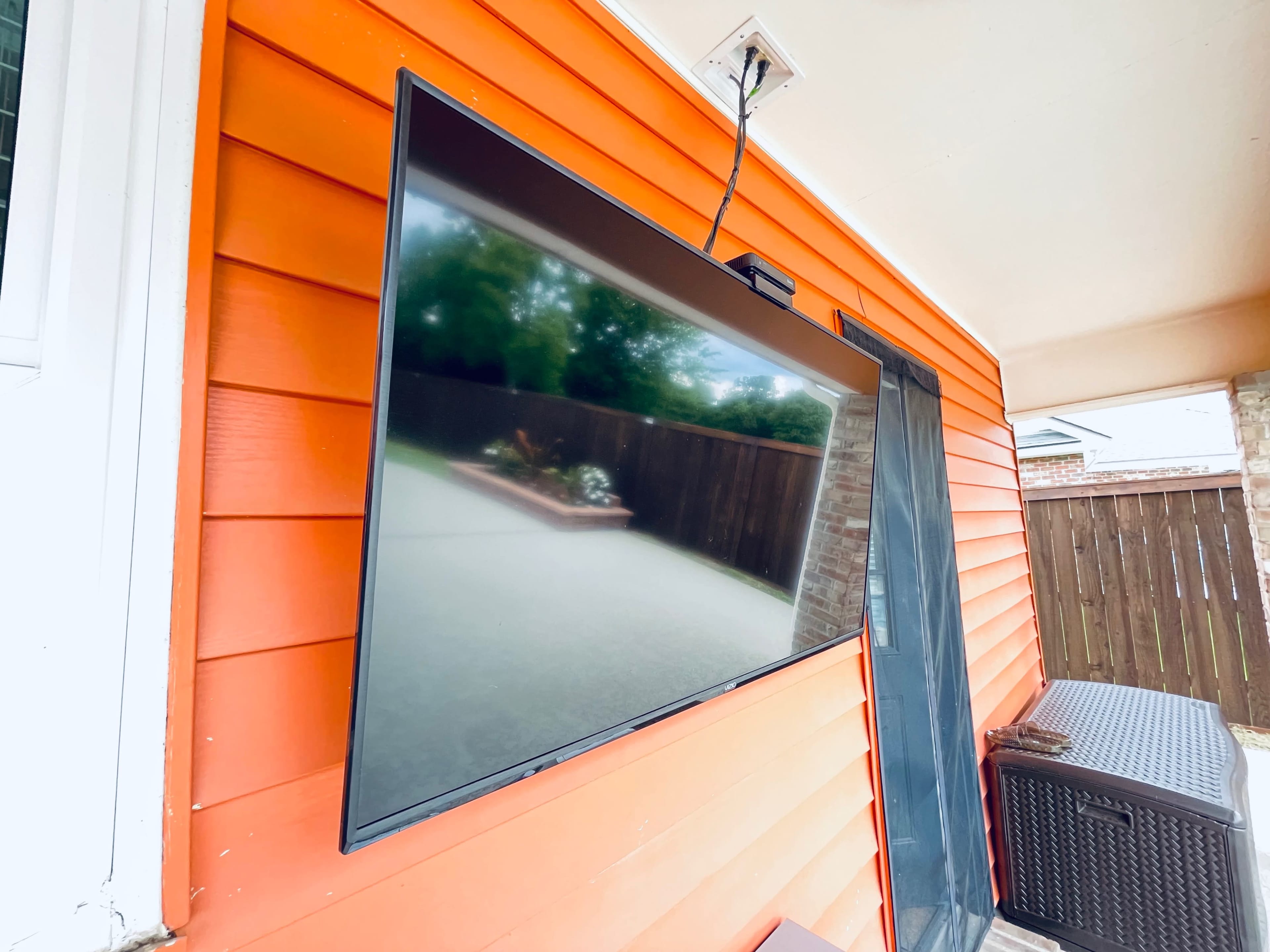A flat-screen television is mounted on an orange exterior wall near a patio area.