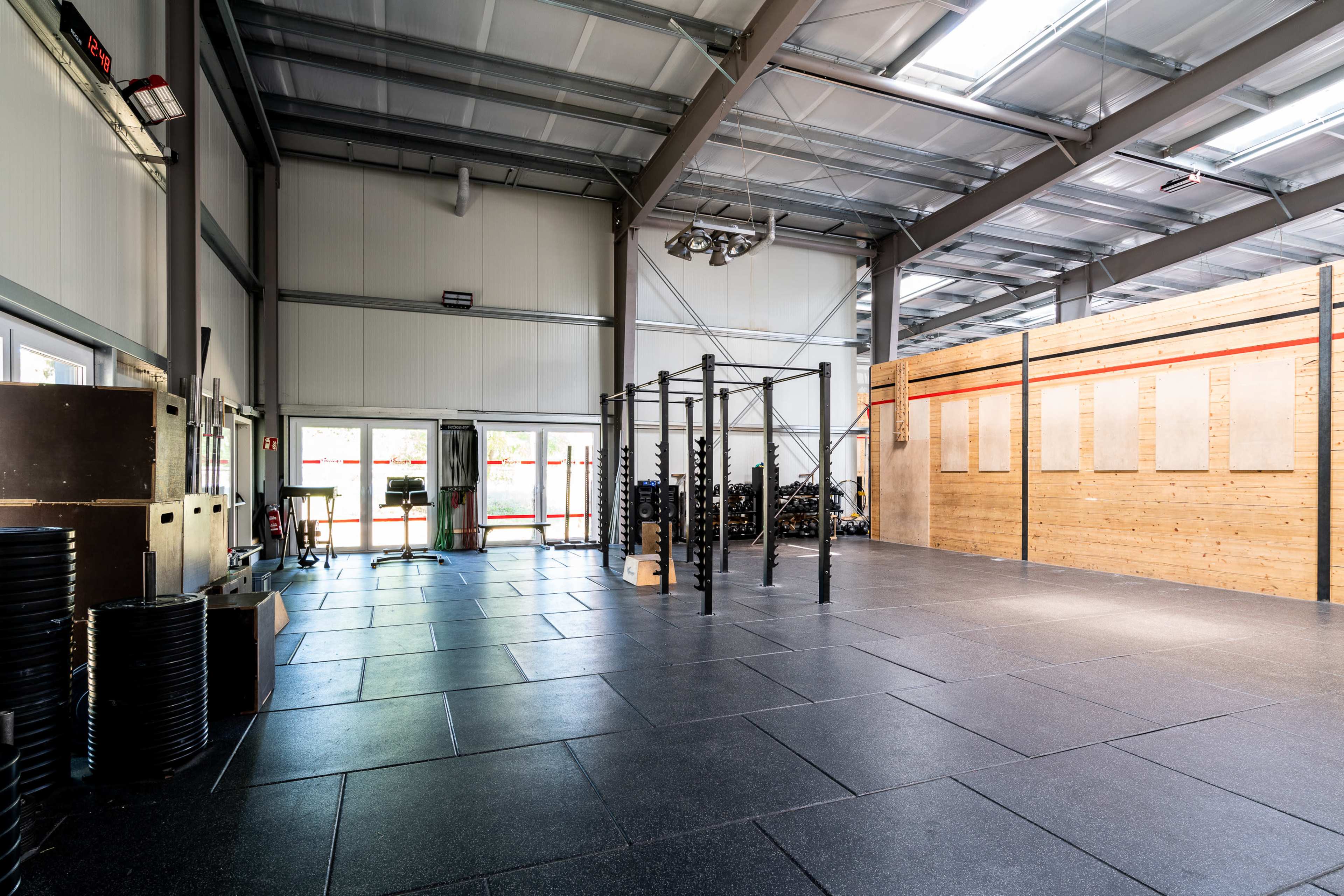 A spacious gymnasium with exercise equipment, including free weights and pull-up bars, in a well-lit industrial setting.