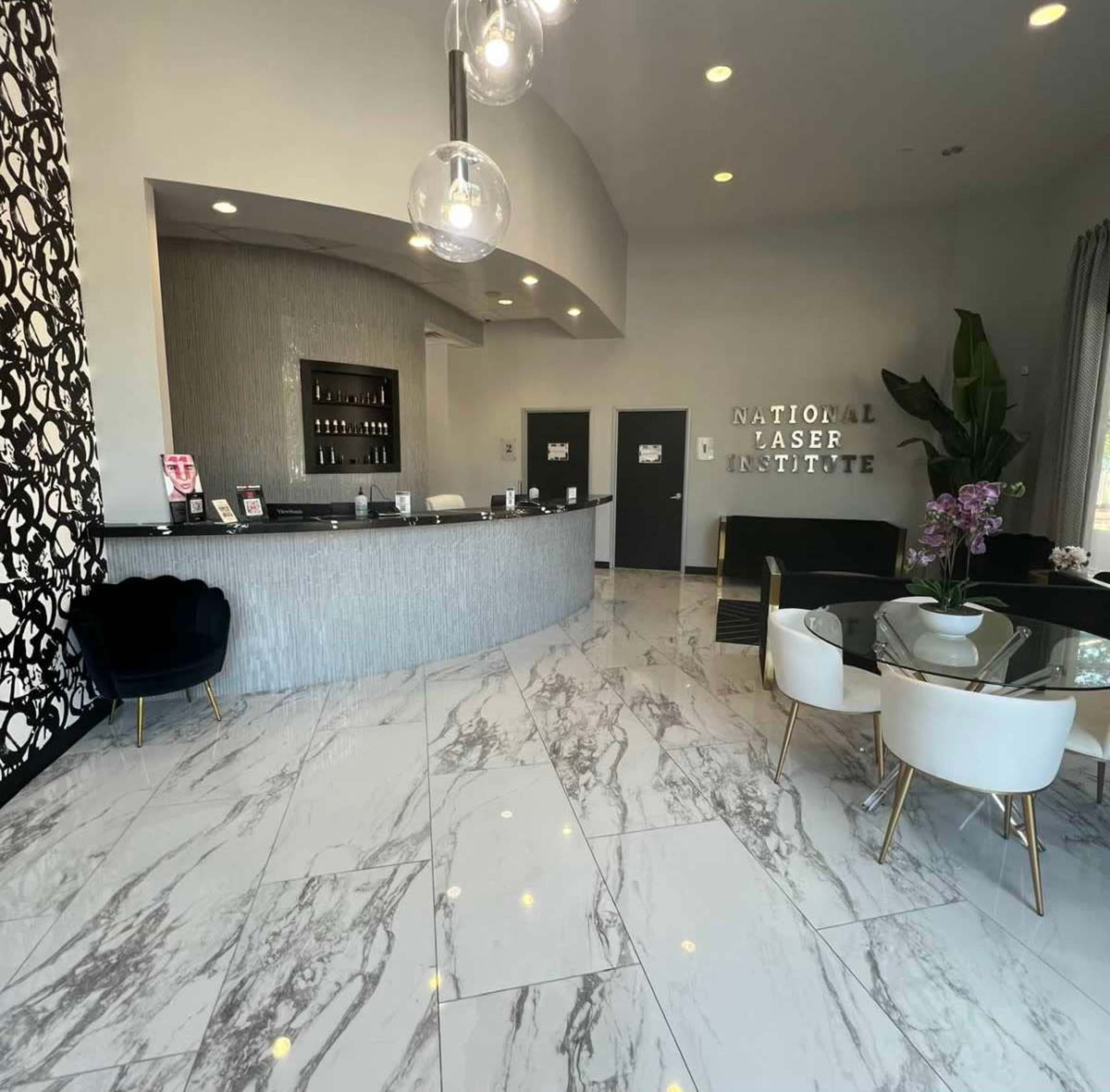The image shows a modern reception area of a laser institute with a sleek front desk, marble flooring, and elegant seating arrangements.